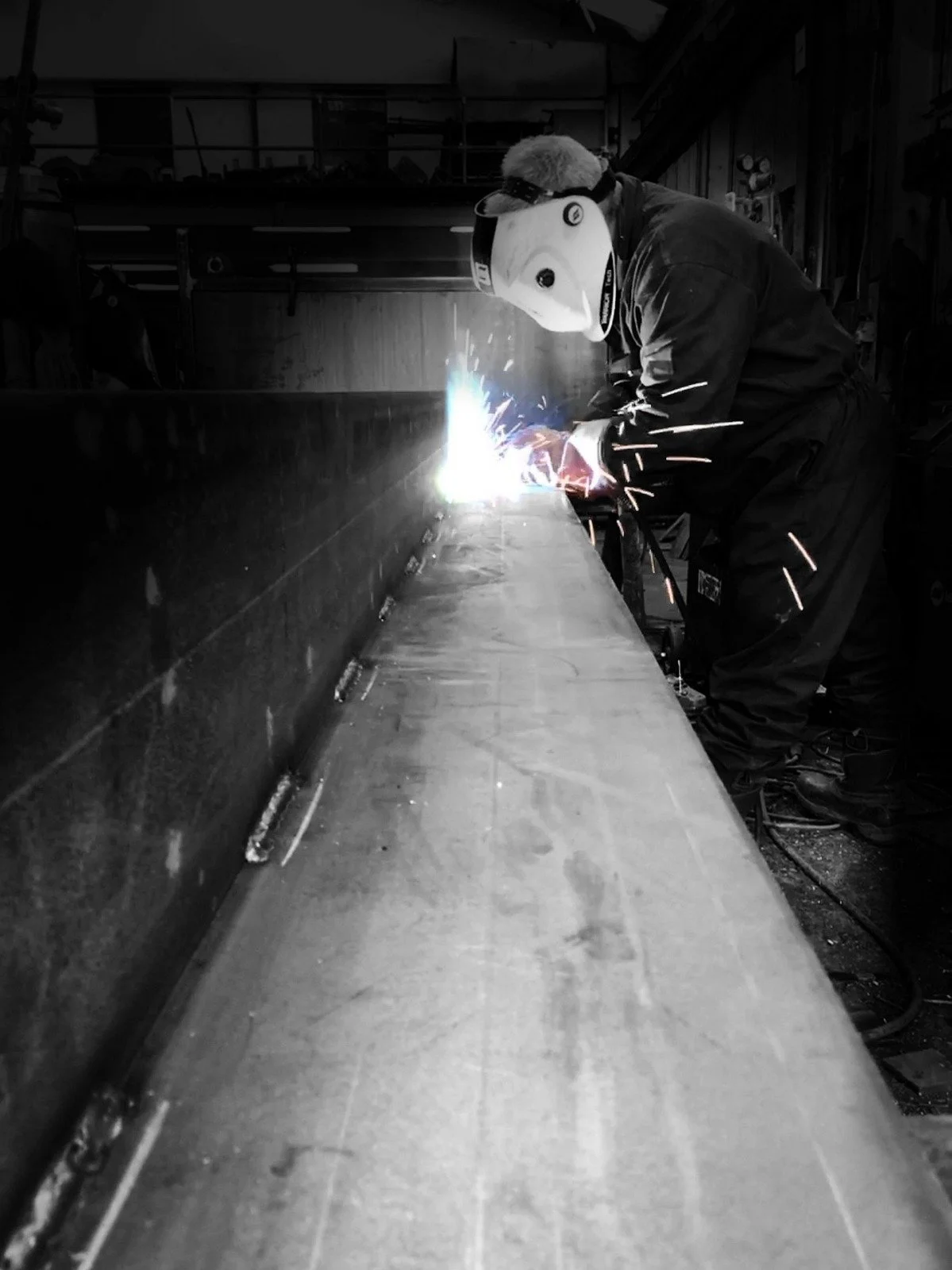 Trabajador con equipo de protección soldando metal en taller industrial.