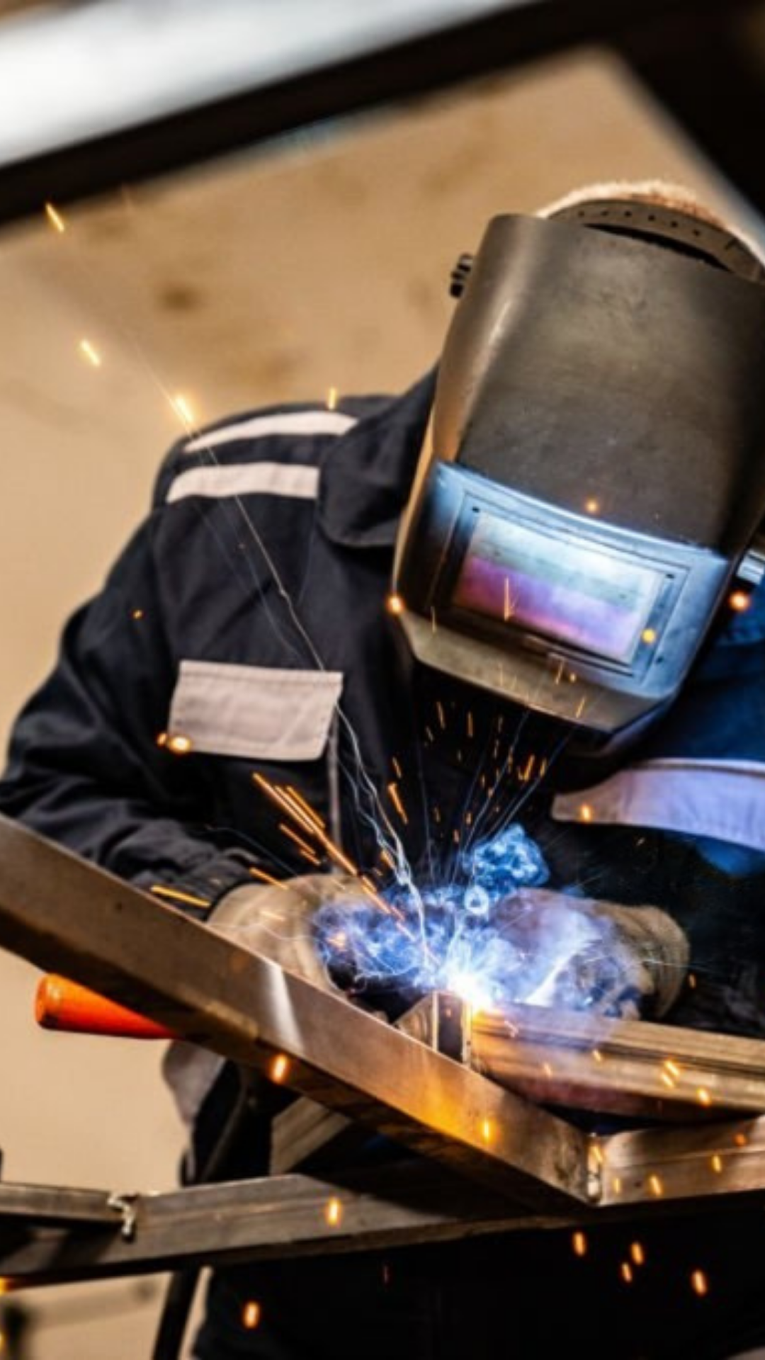 Un soldador con protección facial trabajando en soldadura, con chispas y humo.