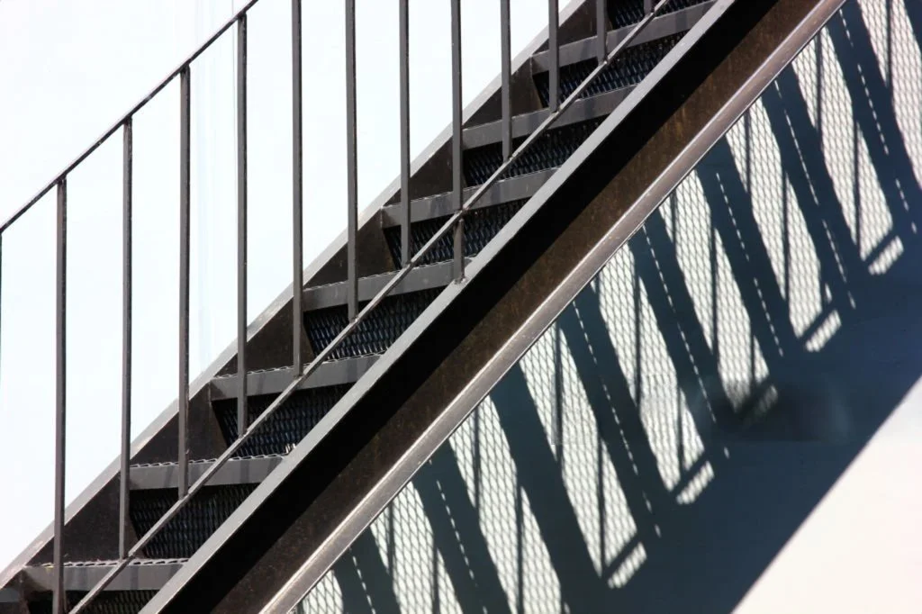 Escalera de metal con sombra que crea un patrón en la pared blanca.