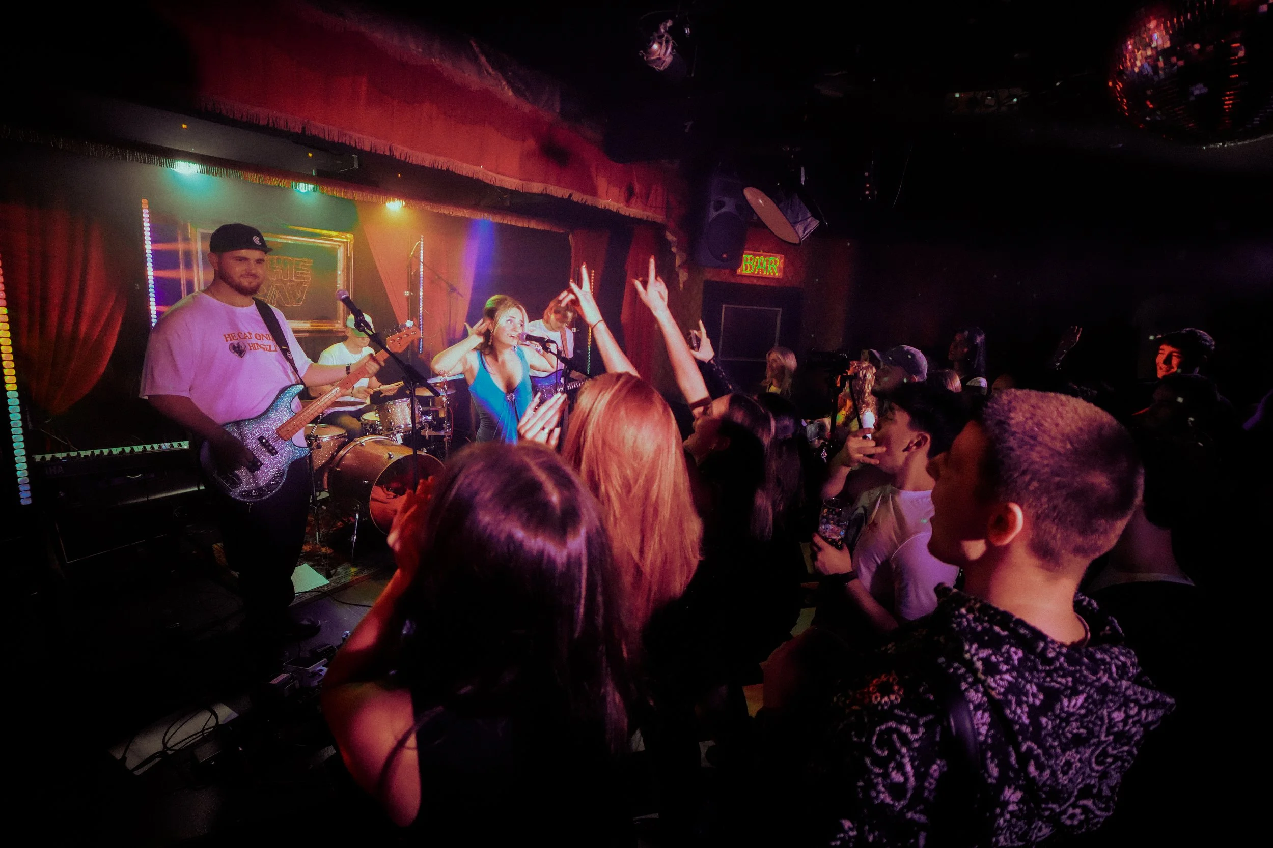 A lively concert scene with a band performing on stage, including a female singer and musicians, with an audience dancing and enjoying the music in a dimly lit venue.