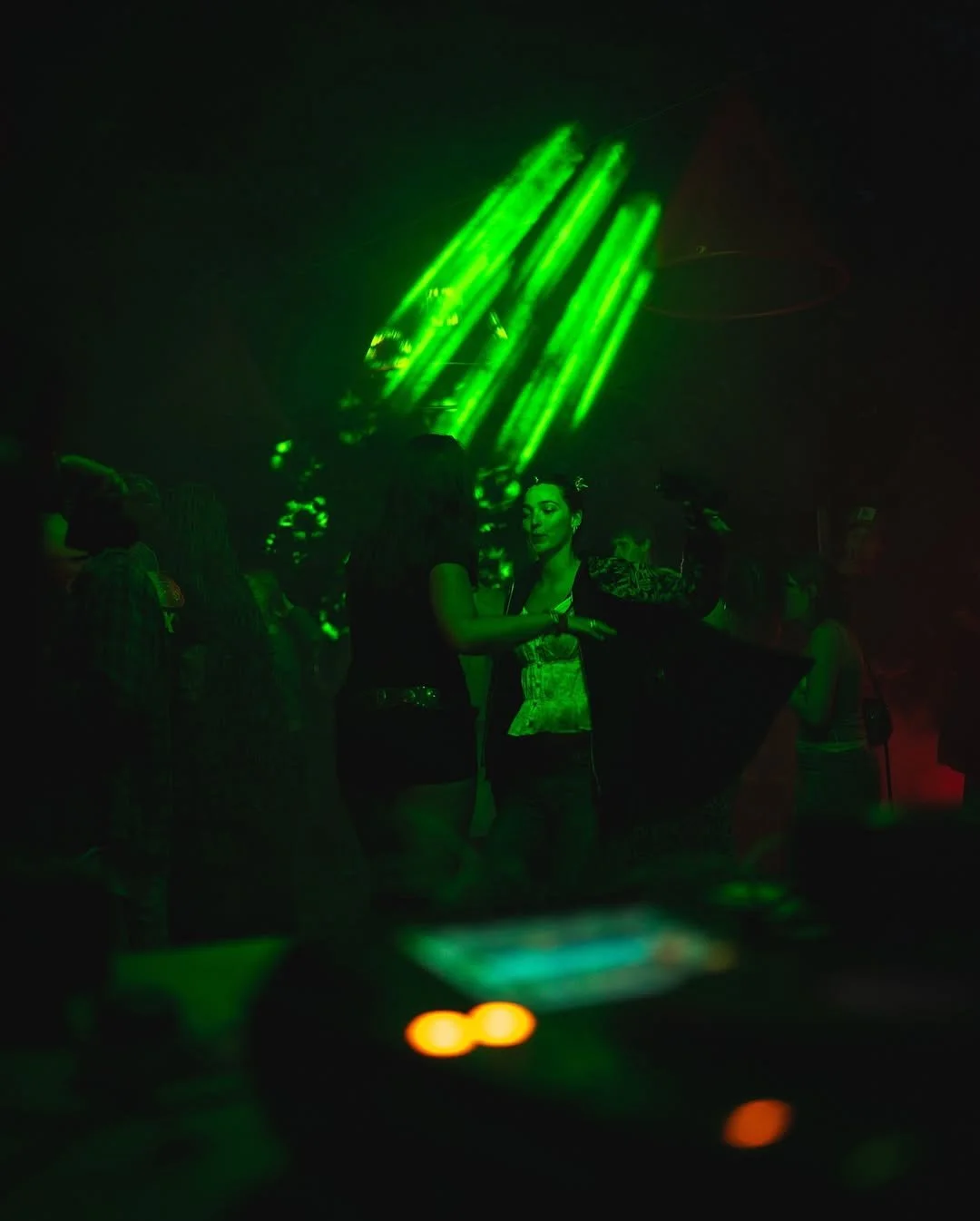 People dancing at a nightclub under green laser lights with a dark background.