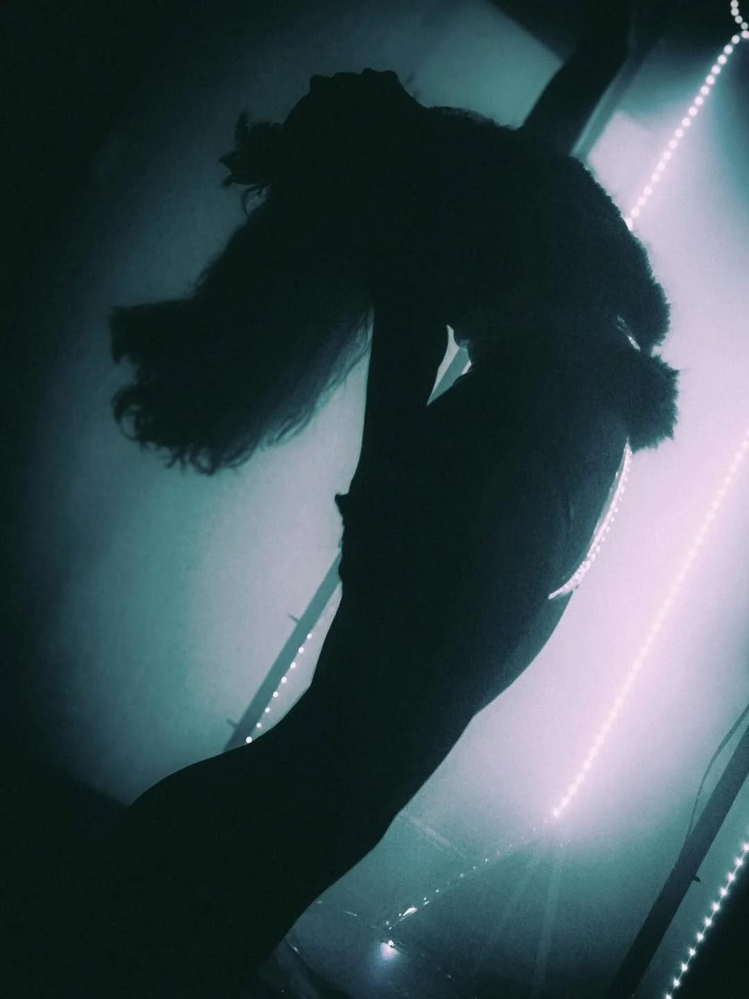 Silhouette of a person with long hair, facing downward in a dimly lit room with blue and purple lighting and LED strip lights.