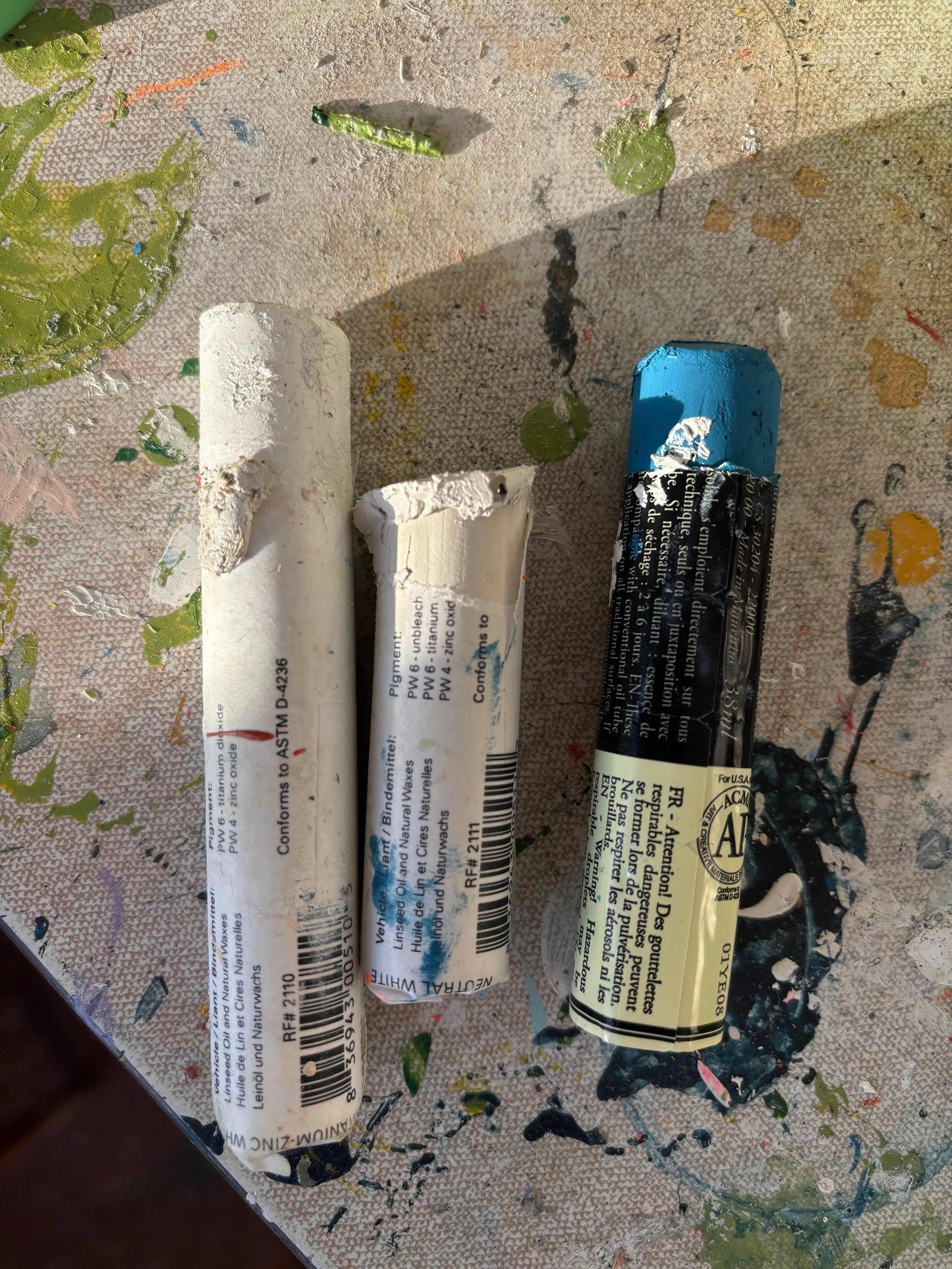 Three tubes of paint on a splattered, colorful surface.