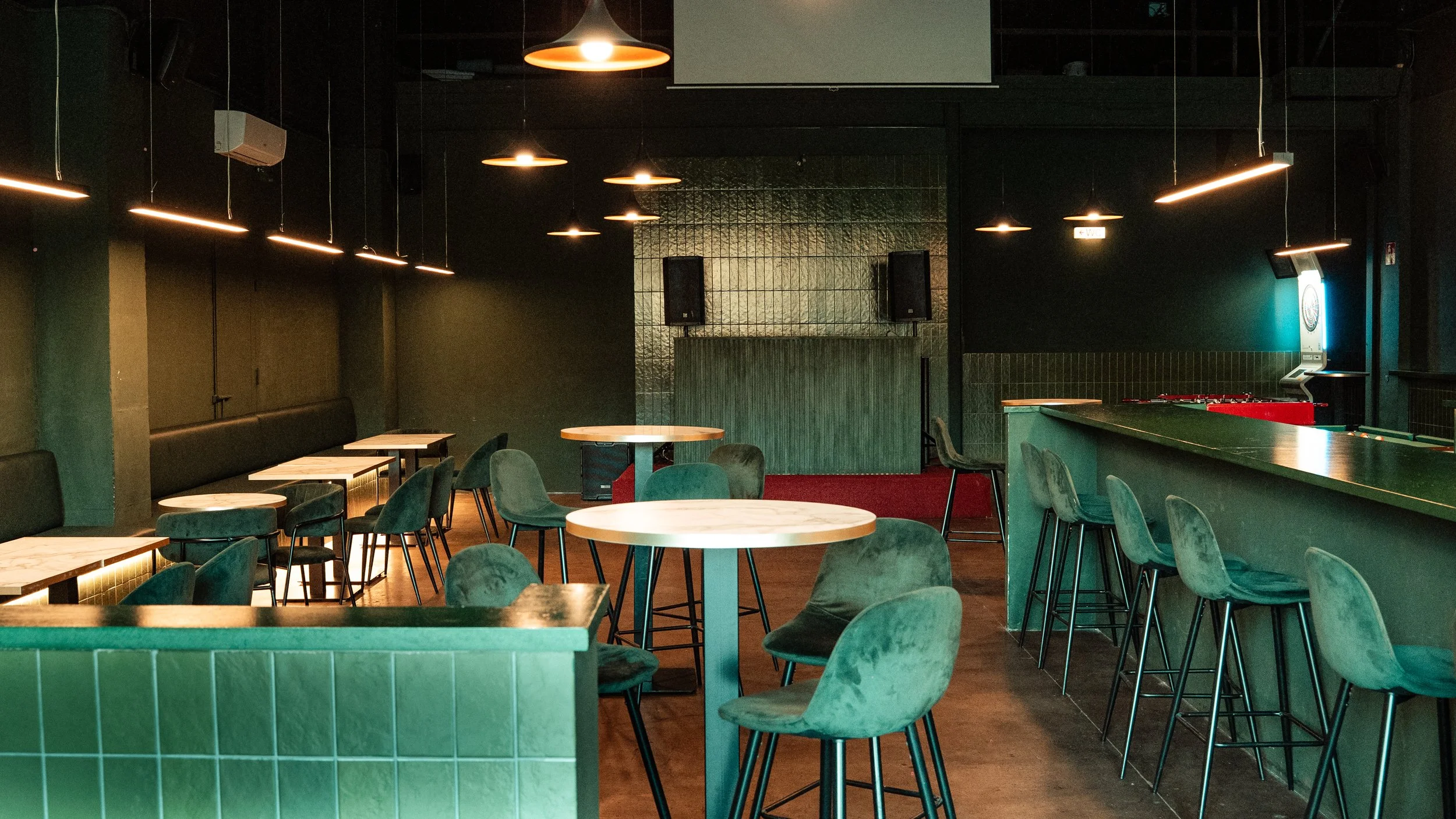 Interiores de bar o restaurante con mesas de mármol, sillas verdes de terciopelo y bar con taburetes, iluminación cálida y ambiente moderno