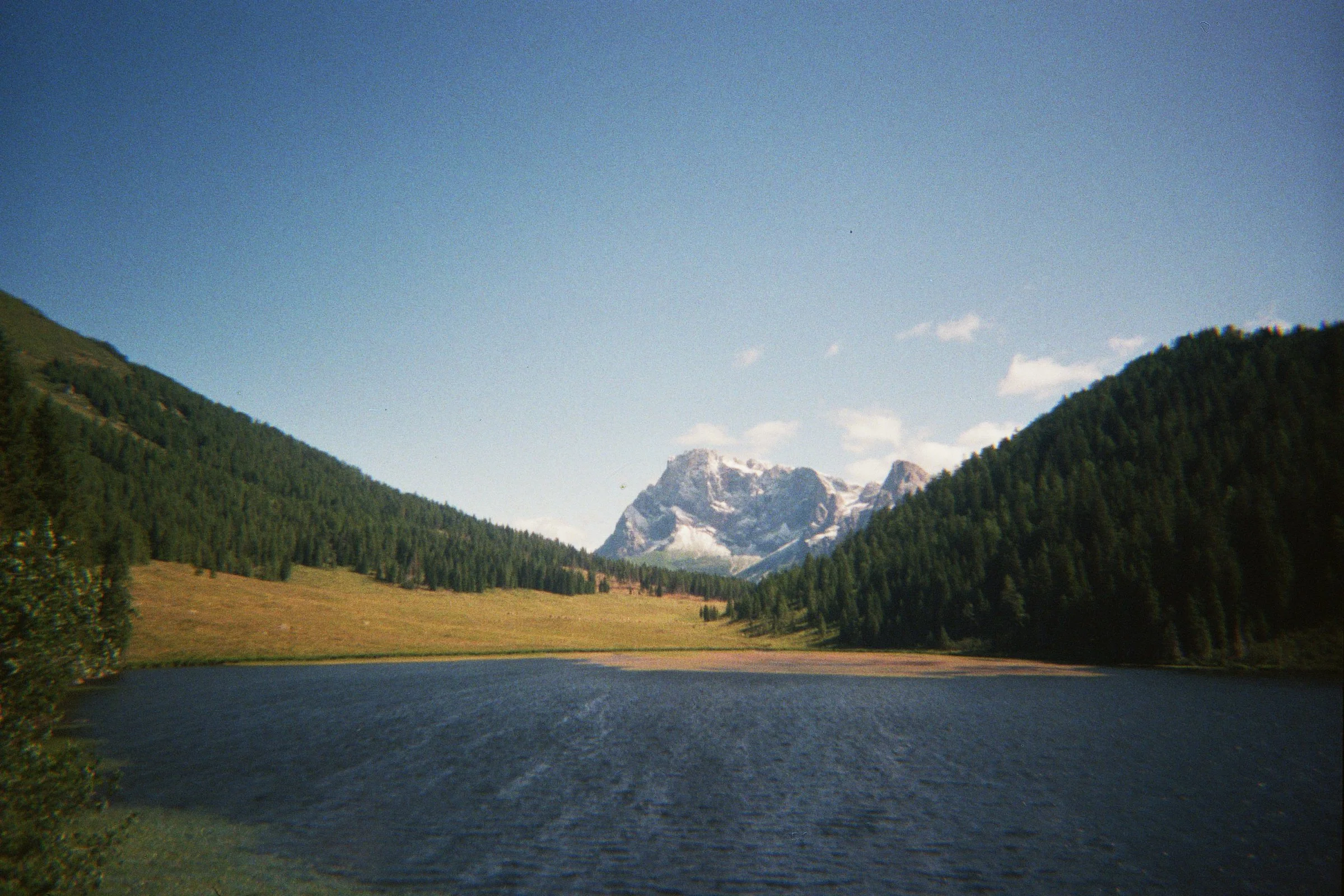 A lake surrounded by lush green trees with mountains in the background and a clear blue sky.