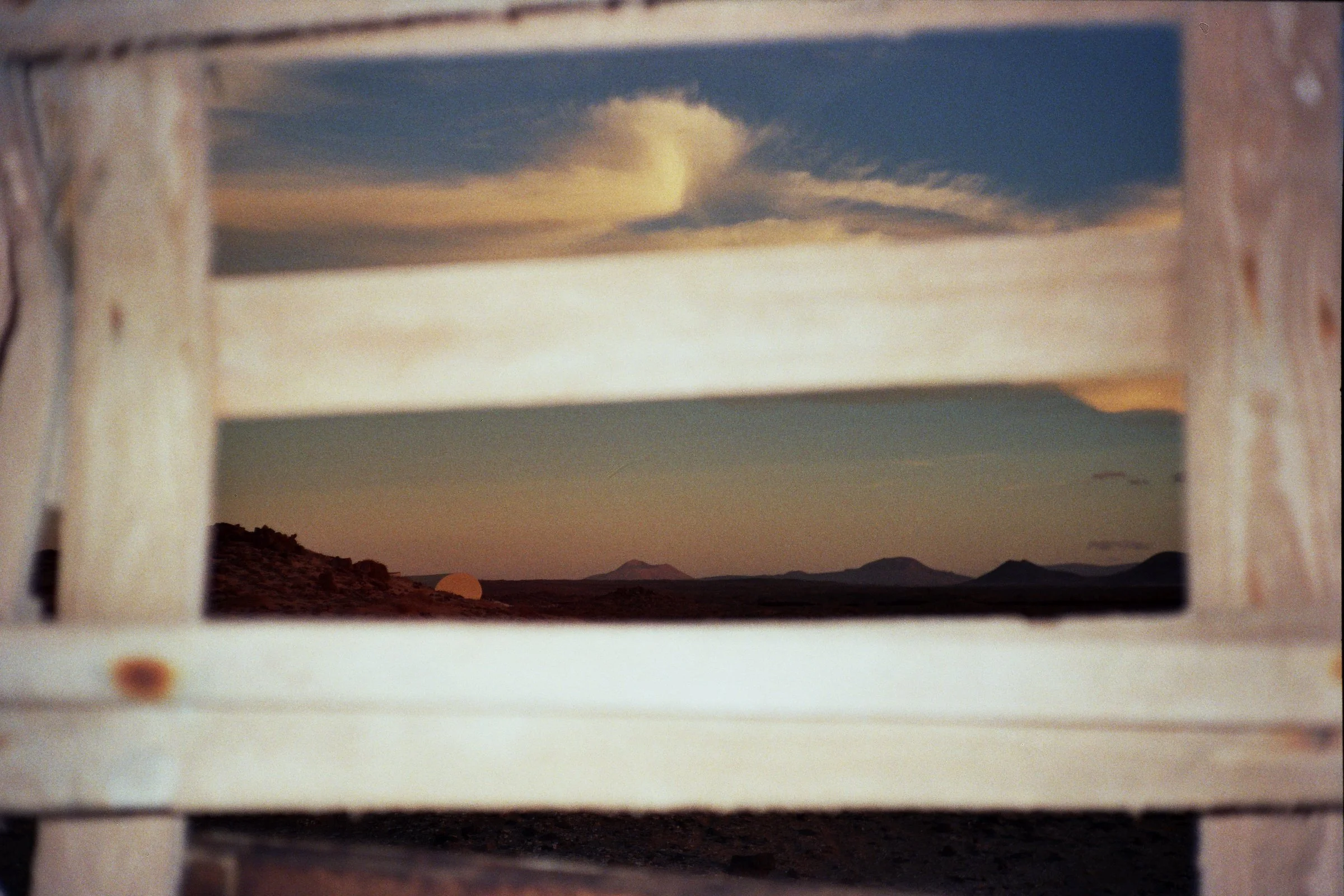 View of a sunset or sunrise horizon with mountains through a rectangular opening in a light-colored wooden structure.
