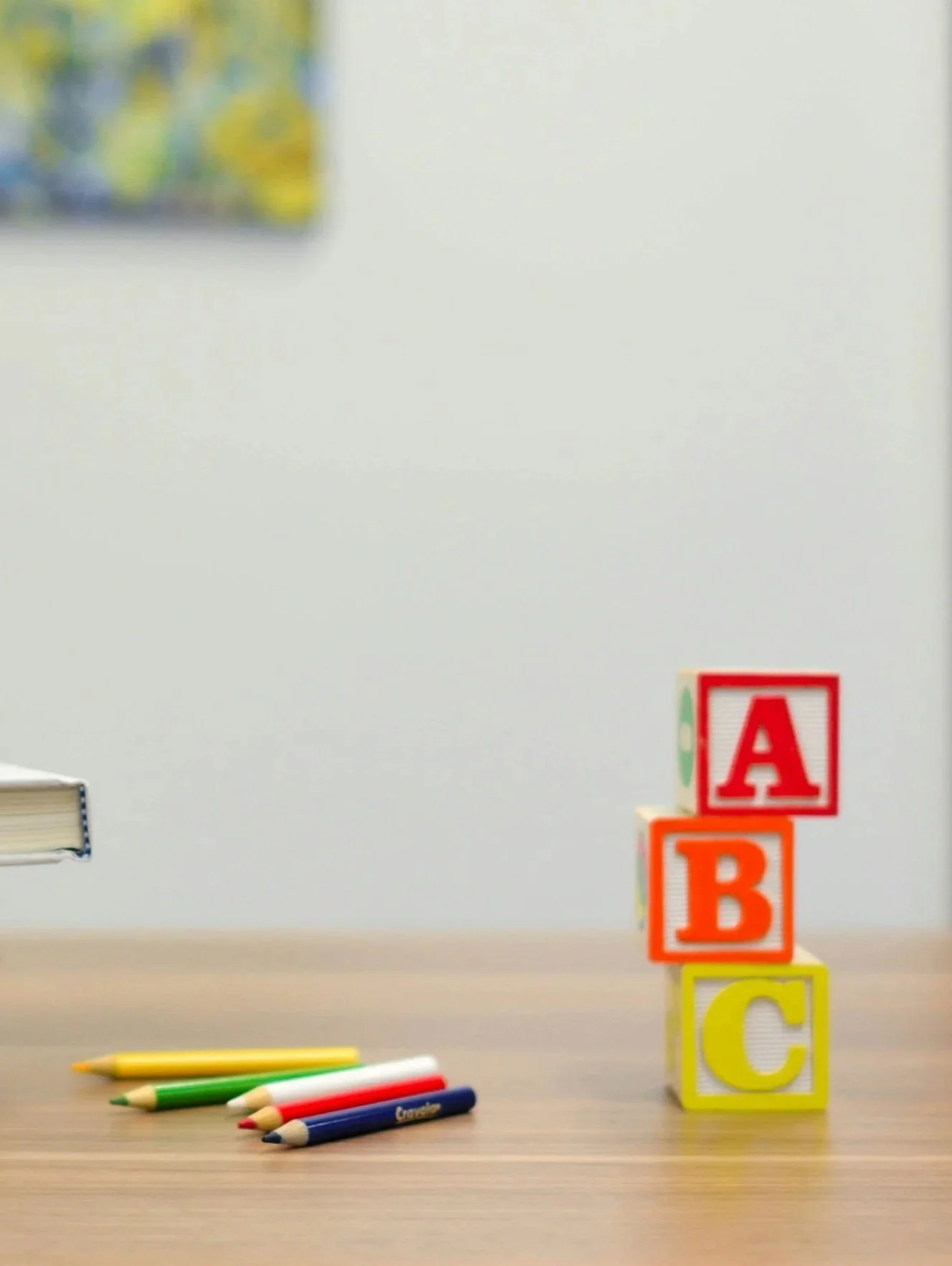 Colorful children's blocks with the letters A, B, and C stacked on a table with four crayons nearby.