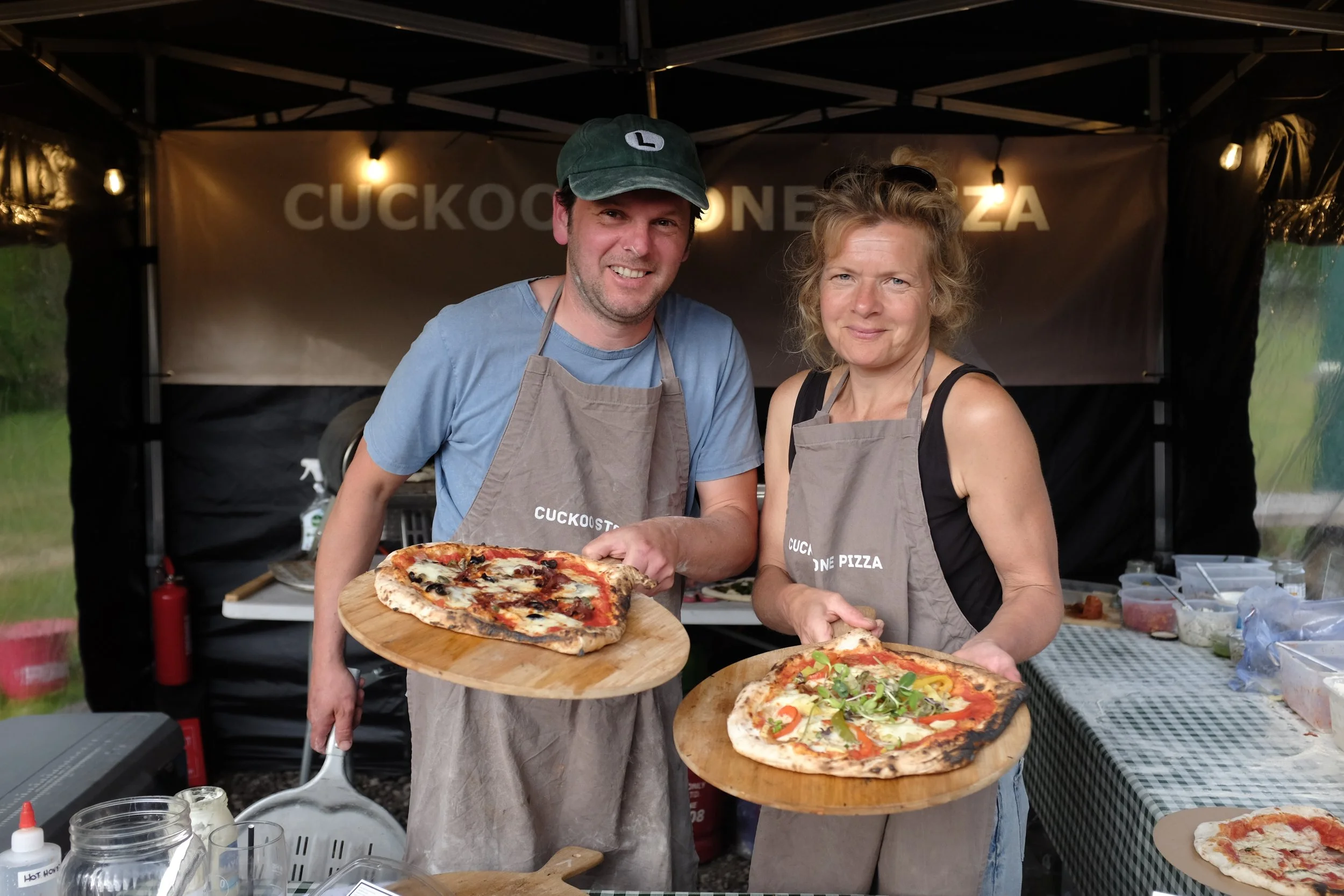 The owners of Cuckoo Stone Pizza holding two freshly made pizzas.