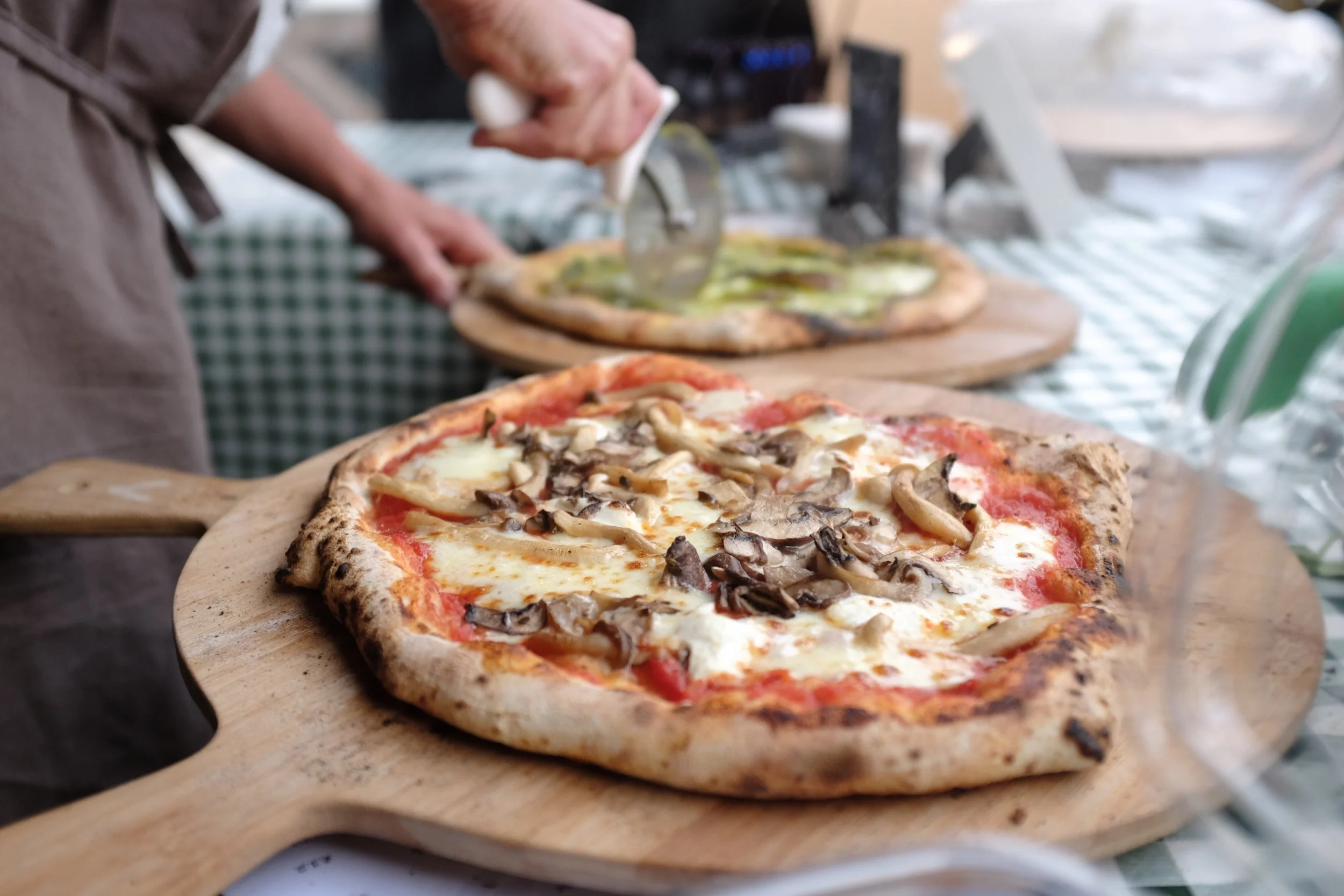 Two artisan pizzas on boards, ready to be cut.