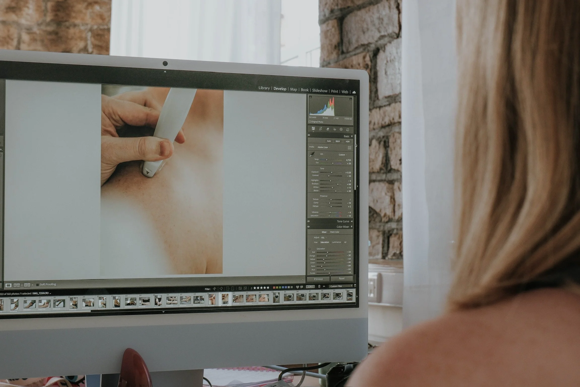 An image of a computer screen at the Not Another Social office in Huddersfield, West Yorkshire. The view of the screen is from over the shoulder of a blonde haired woman. She's editing a photograph.