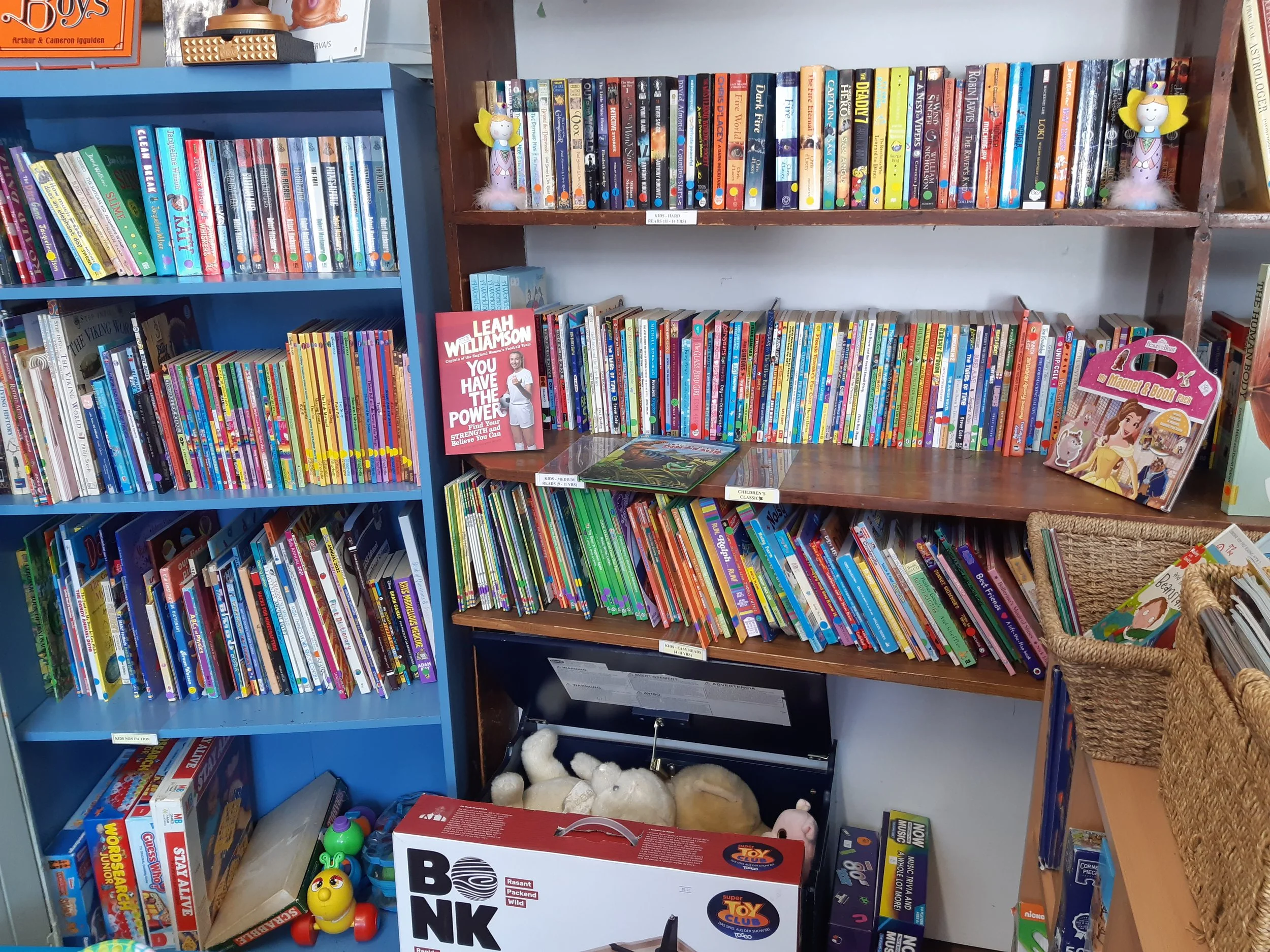 A Marsden bookshop. Bookshelves filled with children's books, toys, and plush animals inside a store or library. There is a mix of colourful books and some toys on display.
