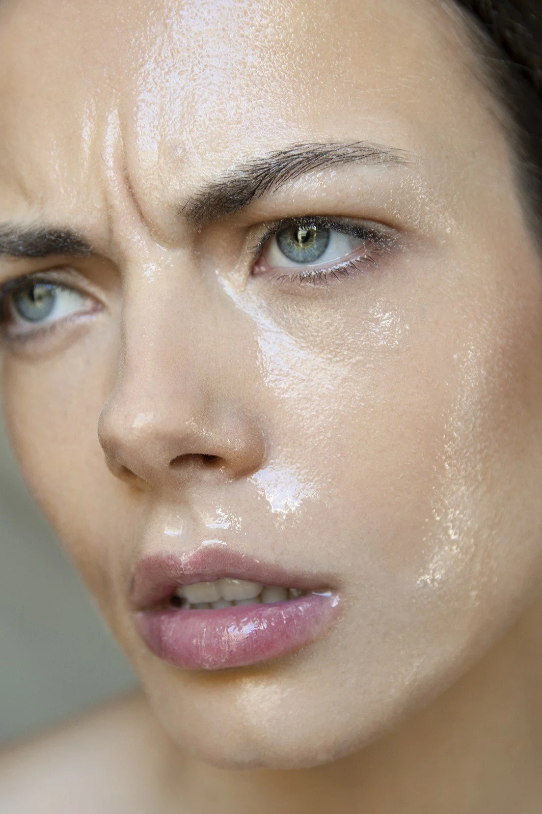 Close-up of a woman with wet skin and water droplets on her face, looking intently to the side.