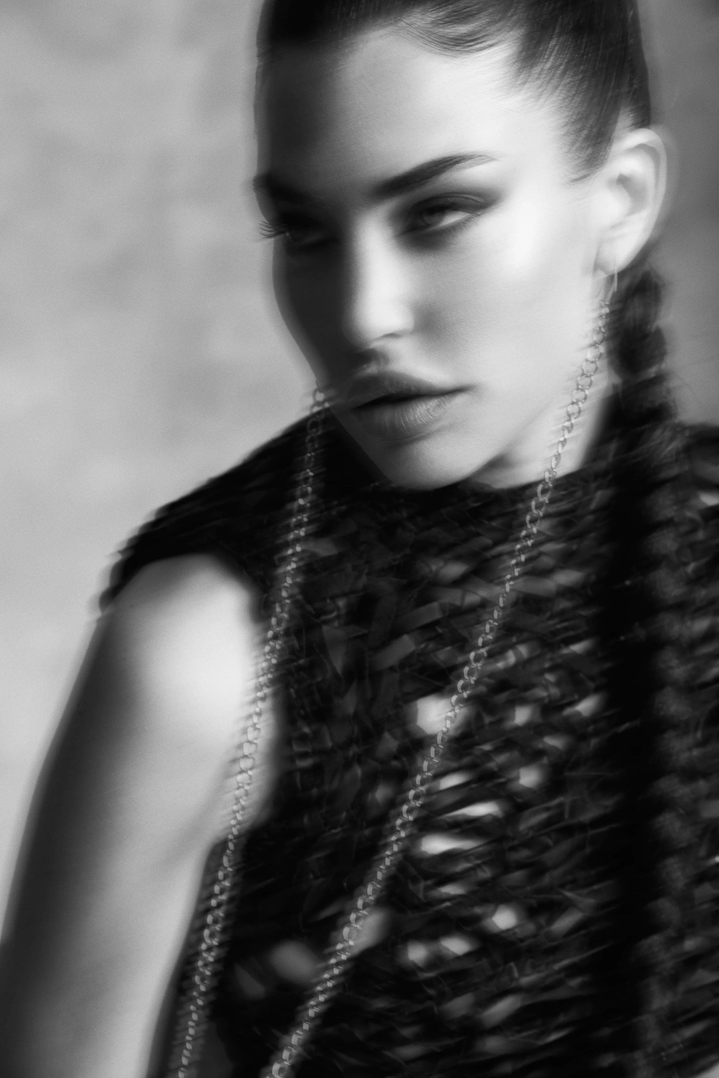A black and white close-up portrait of a woman with her eyes slightly closed and lips parted, wearing a textured top and long necklace.