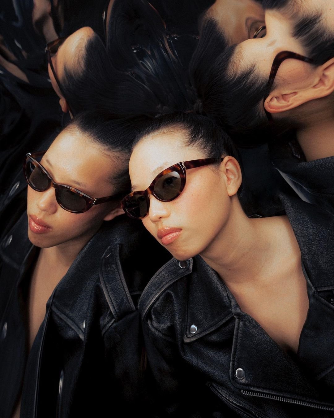 Three women lying on the floor, wearing black leather jackets and sunglasses.