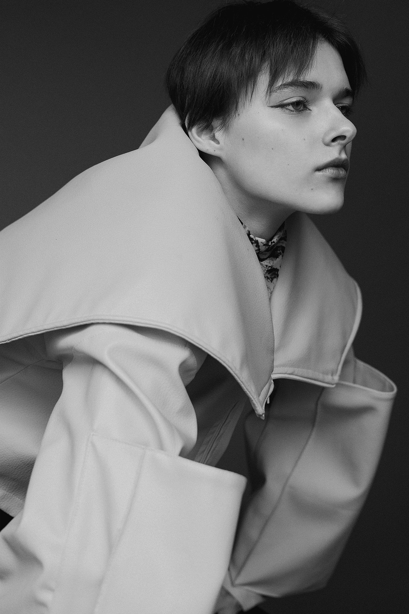 Black and white portrait of a woman with short hair wearing a large, structured jacket and patterned top underneath.