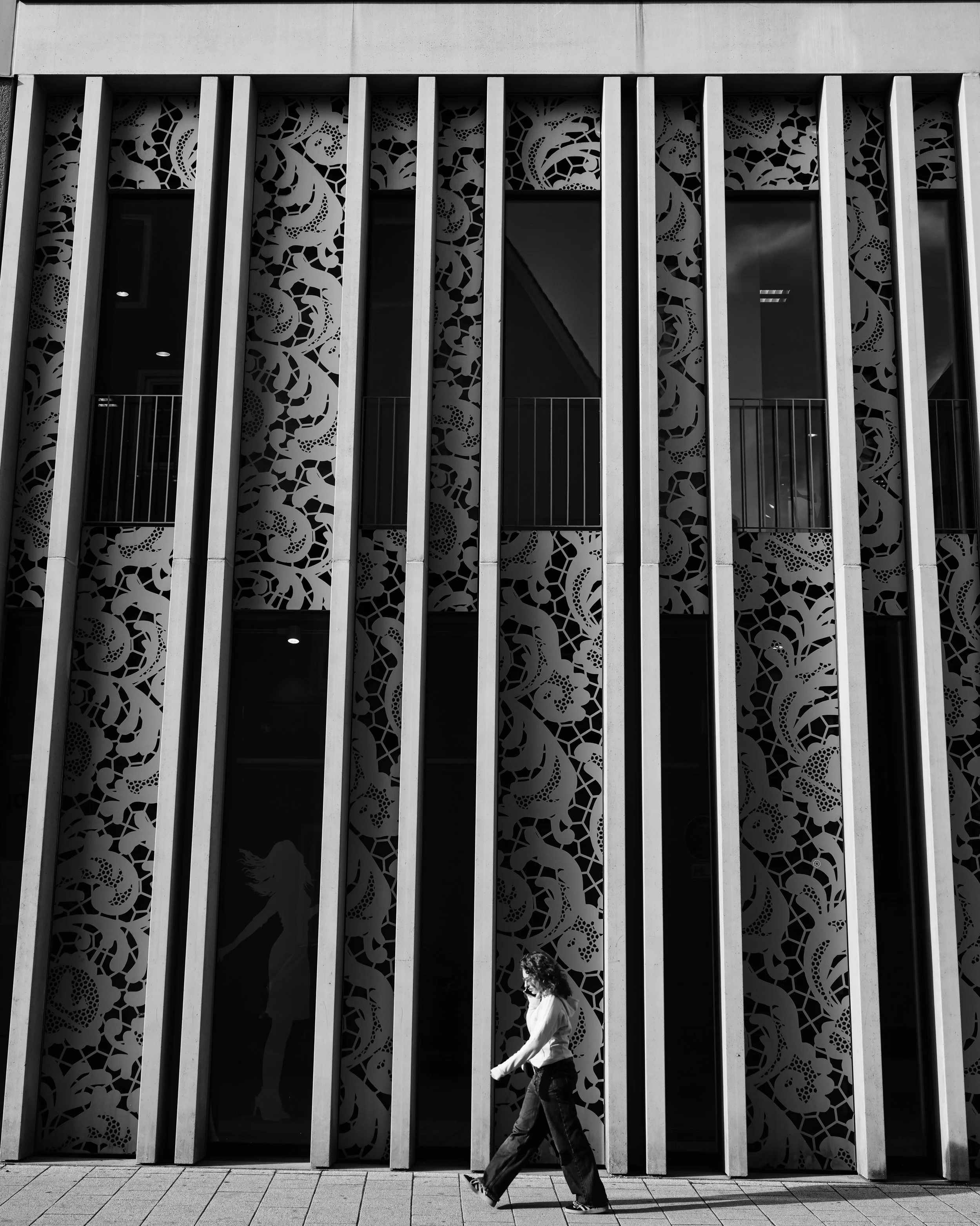 Frau läuft vor einem modernen Gebäude mit kunstvoll gestalteten Fenstern und senkrechten Zierelementen.