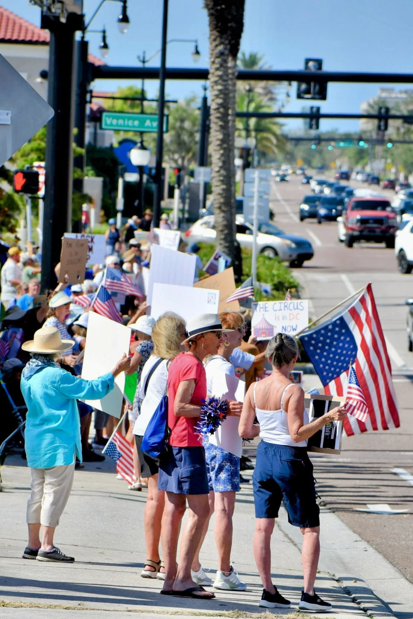 People protesting with American flags and signs on a city street on a sunny day.