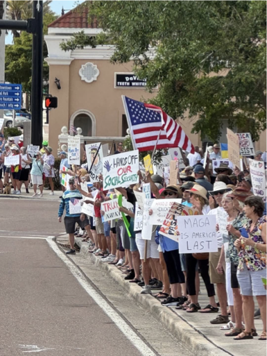 Group of protestors holding signs and an American flag on a sidewalk during a demonstration.