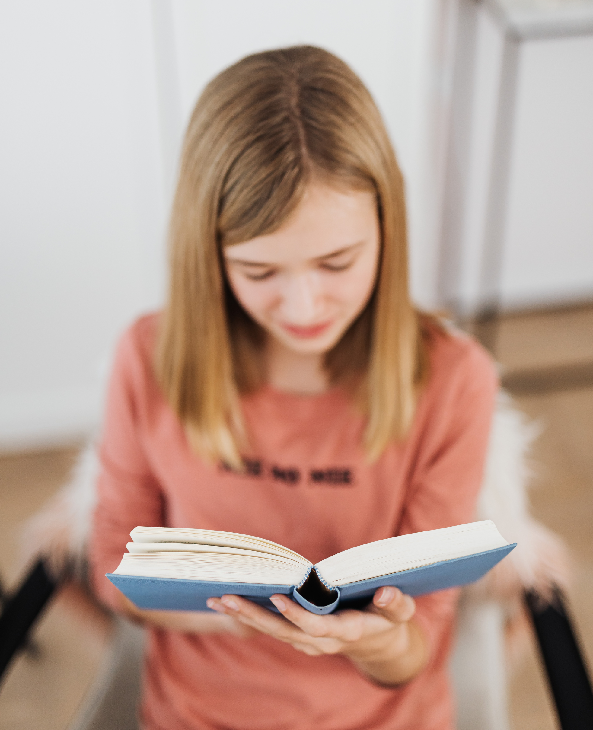 A woman with long blonde hair is holding an open blue book and looking down at it.