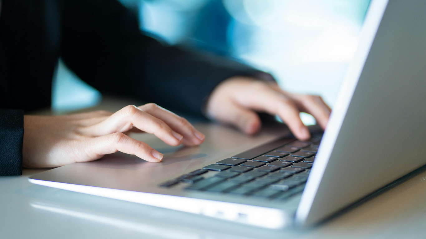 Person typing on a laptop with a black blazer.