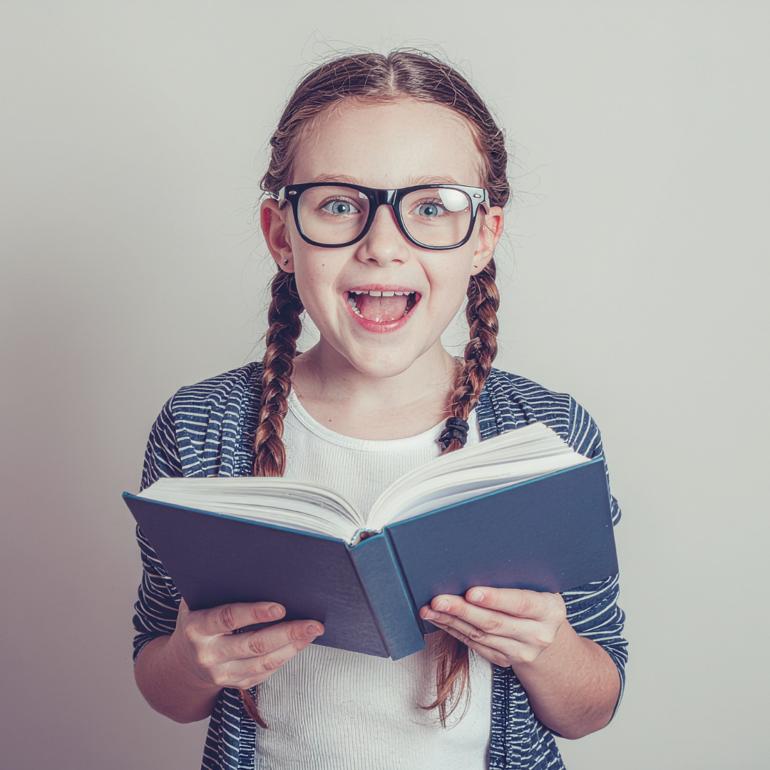 A young girl with braided hair, glasses, and a striped cardigan reading a book with a surprised or excited expression.
