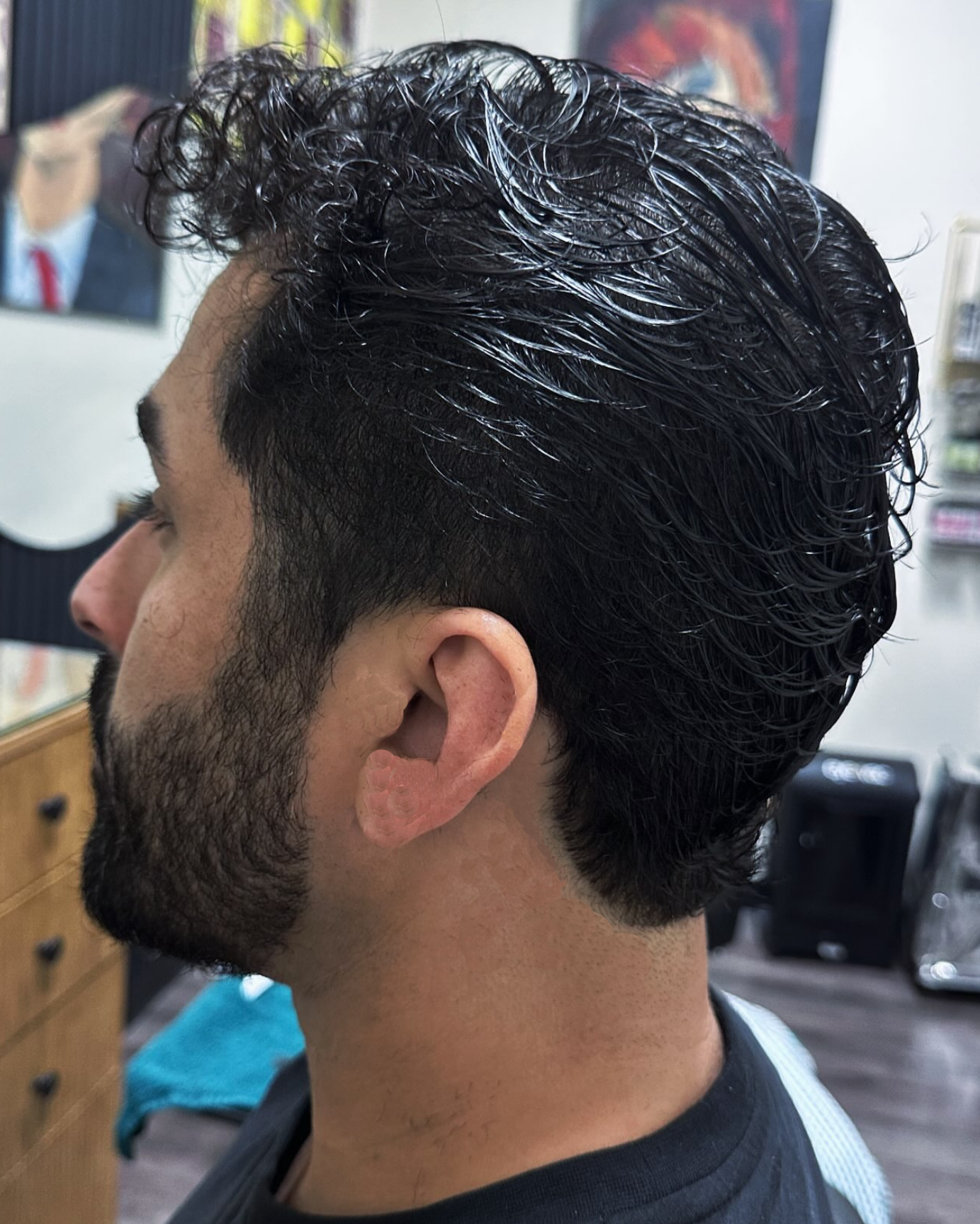 A man with dark, wet, curly hair and a beard, seen from the side in salon setting.