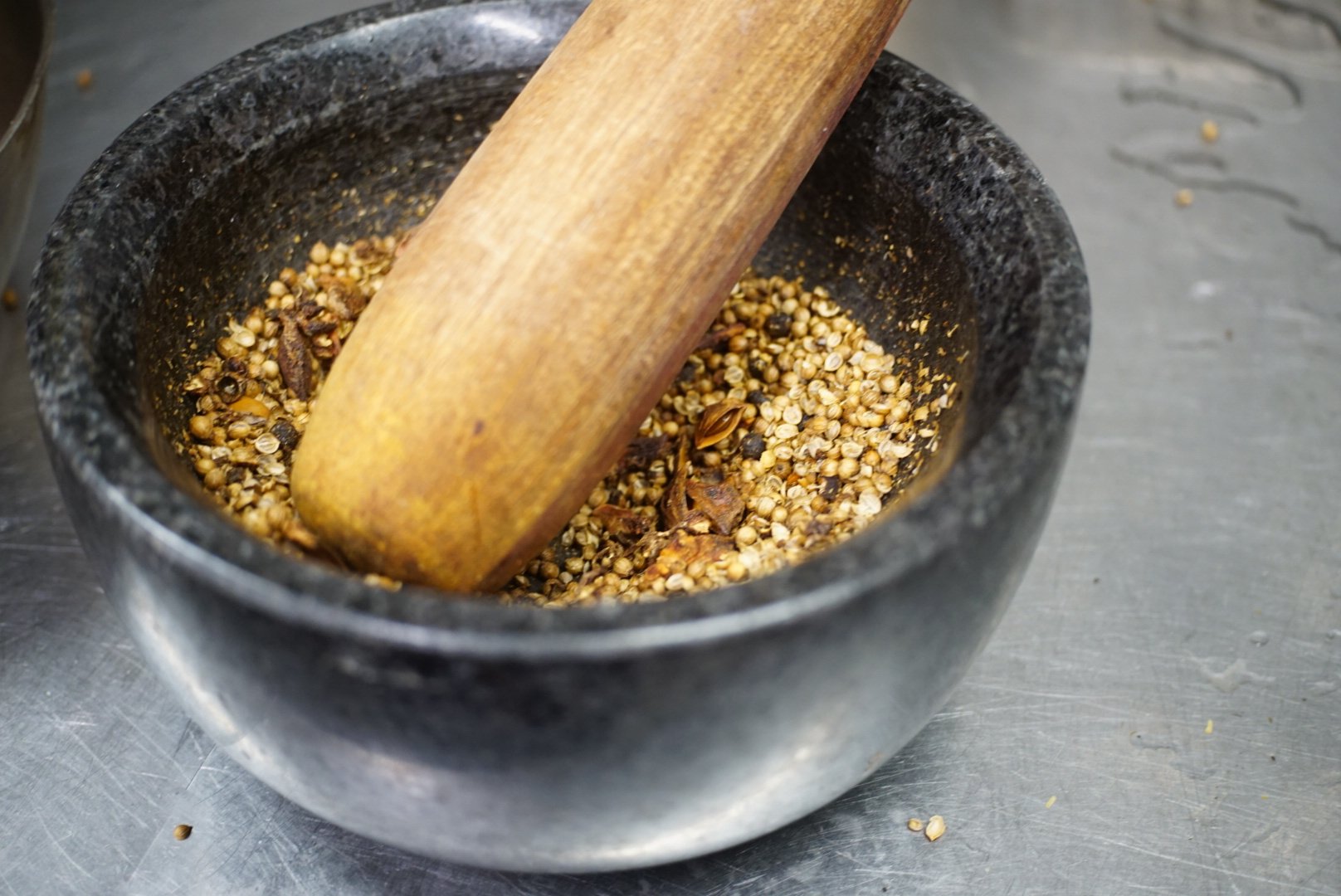 Grinding spices in a black stone mortar with a wooden pestle.