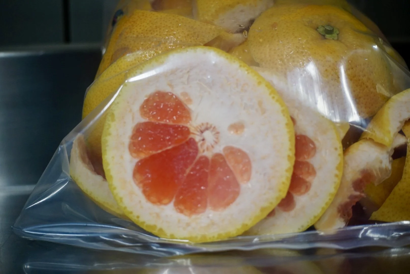Freshly sliced grapefruits in a plastic bag with some whole grapefruits in the background.
