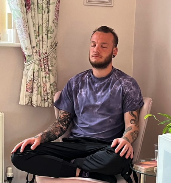 A man with tattoos sitting cross-legged while meditating, representing private one-to-one meditation sessions and personalised spiritual mentoring with Katarina Tilley.