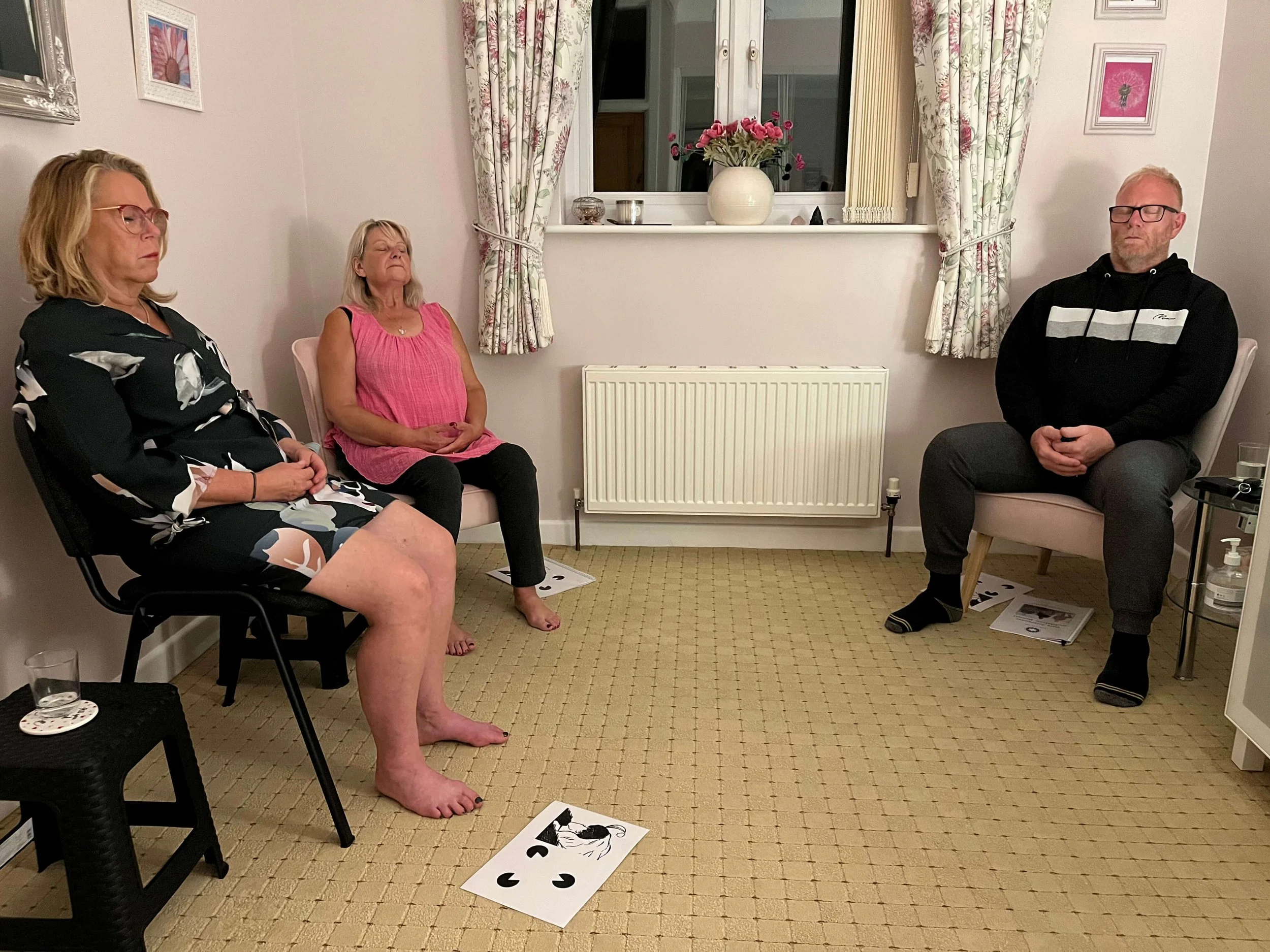 Two women and a man sitting sitting in meditation, during a Mindfulness Meditation Course session with Katarina Tilley, serving clients across Clacton-on-Sea, Colchester, and the wider Essex area.