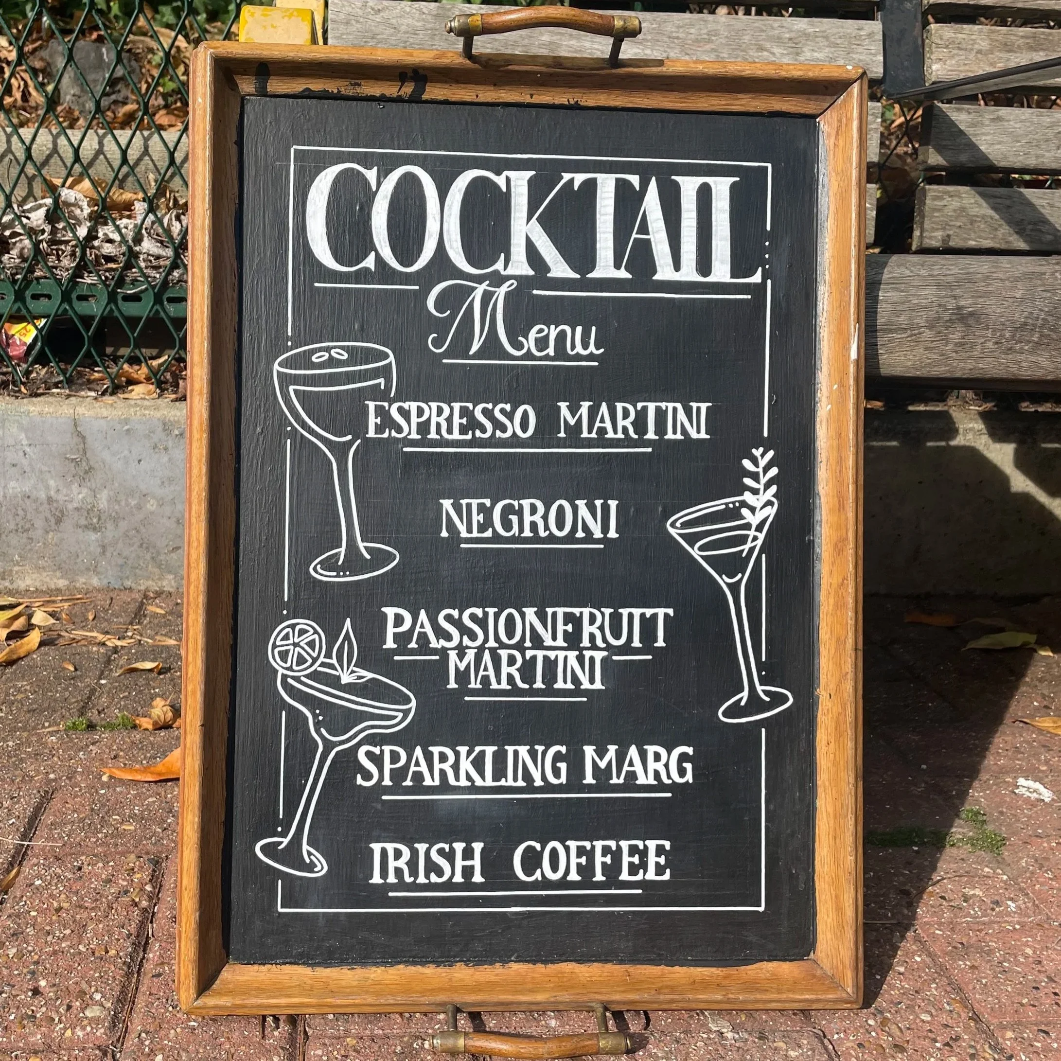 Chalkboard sign outside a restaurant listing cocktail menu items such as Espresso Martini, Negroni, Passionfruit Martini, and Irish Coffee.