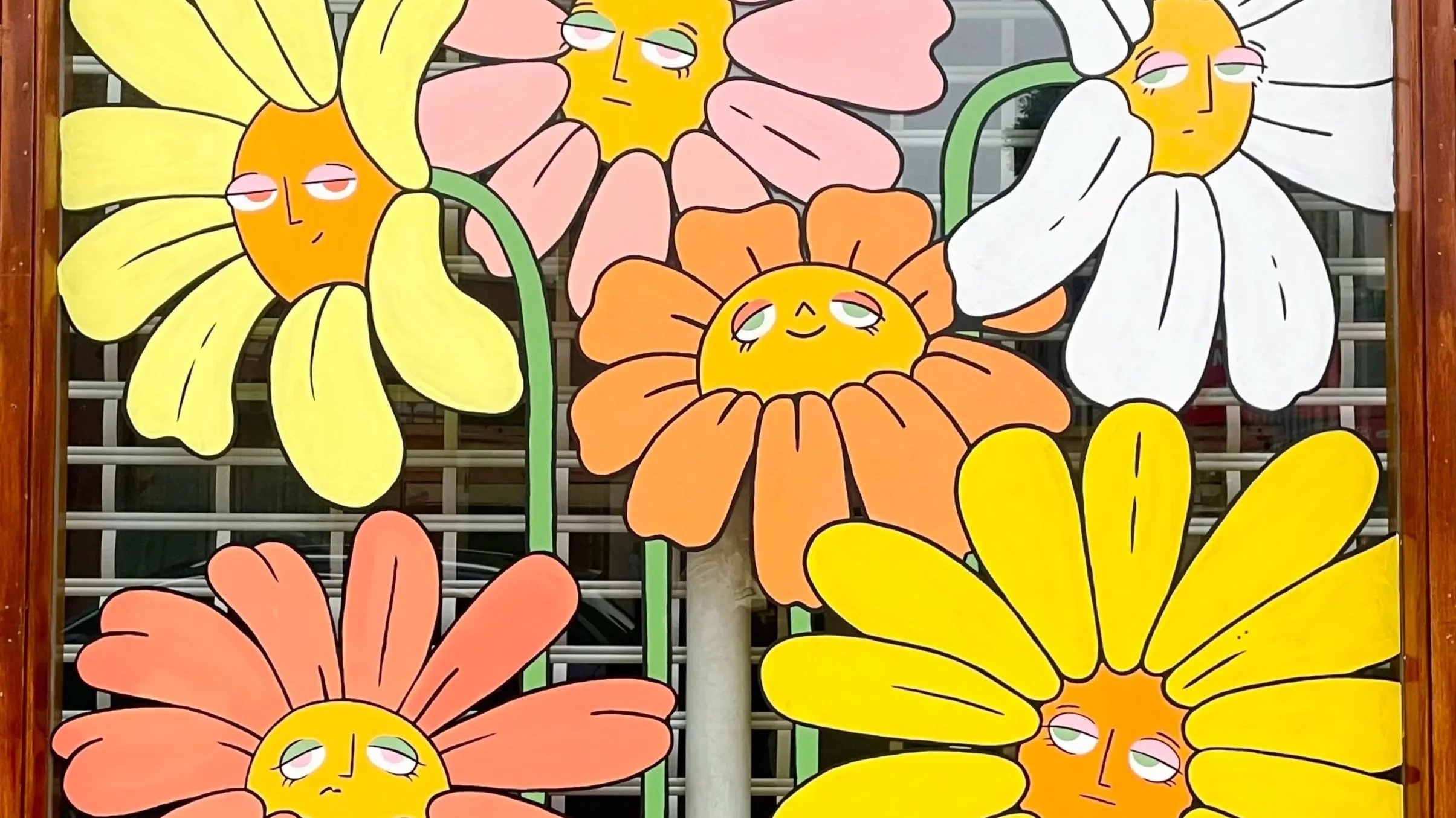 Colorful mural of large, cartoonish flowers with smiling, sleepy sun faces in the center of some flowers and droopy eyes.