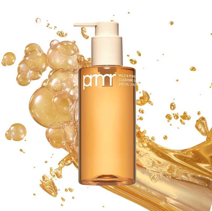 A bottle of pmr Mild & Perfect Cleansing Oil with splashes of golden-colored oil and bubbles around it.