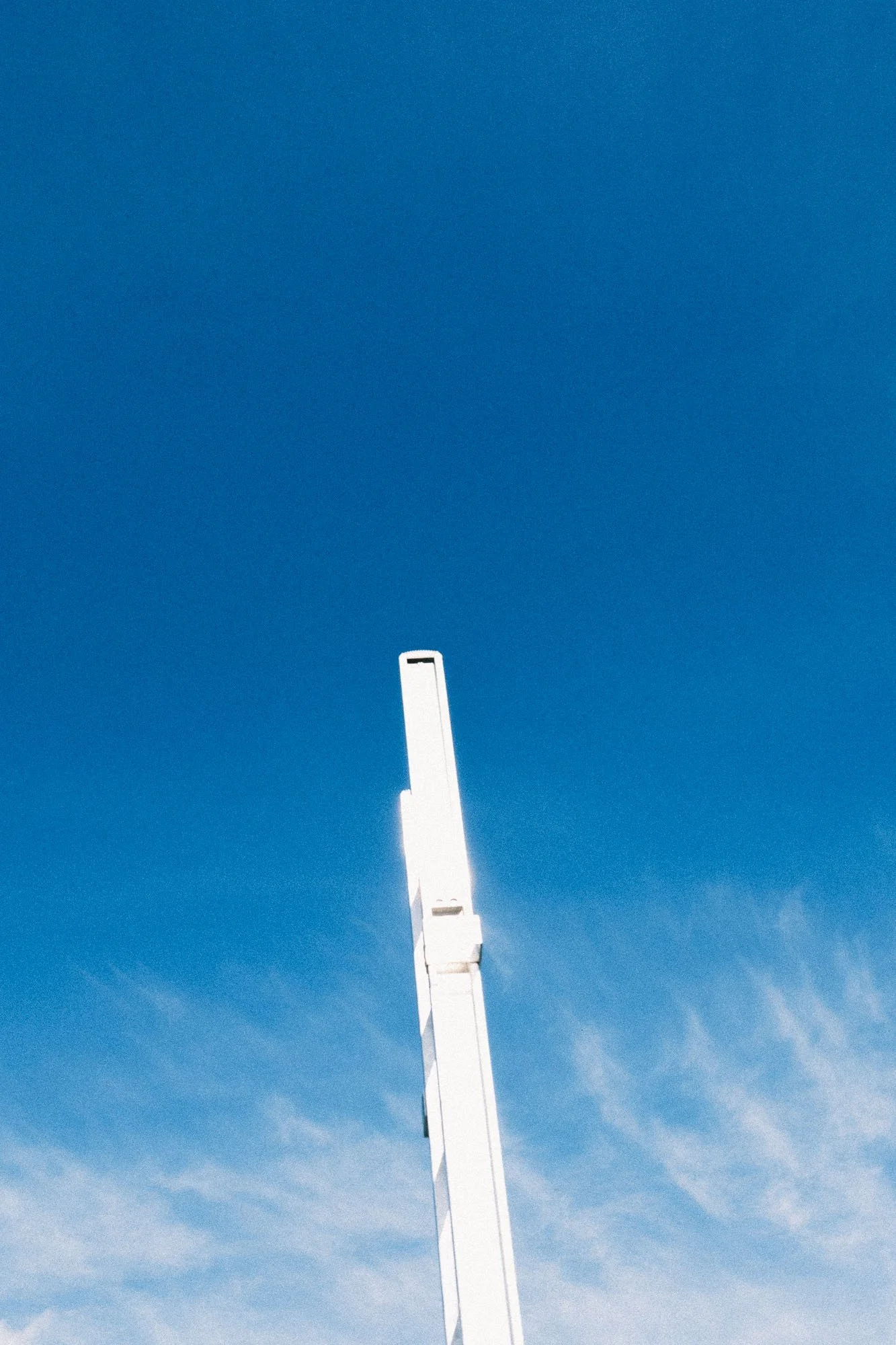 A white telecommunications tower extending into a bright blue sky with a few wispy clouds.