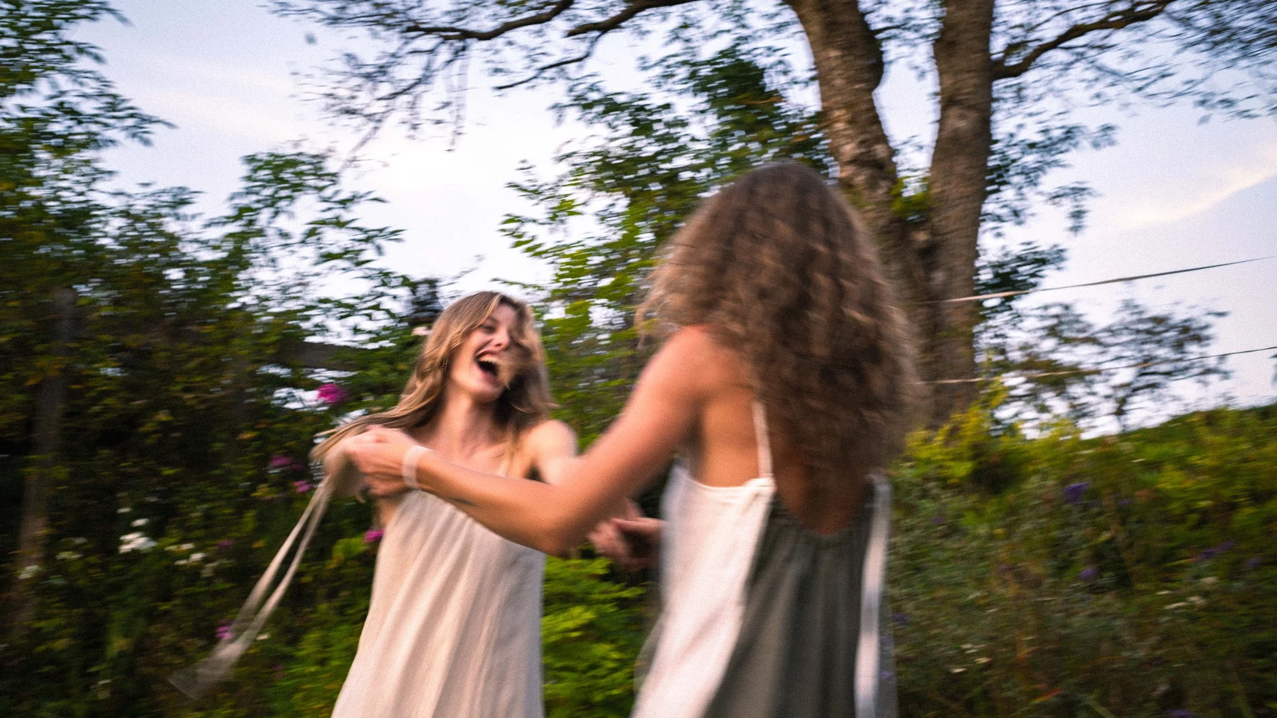 Two women are outdoors, holding hands, smiling, and laughing.