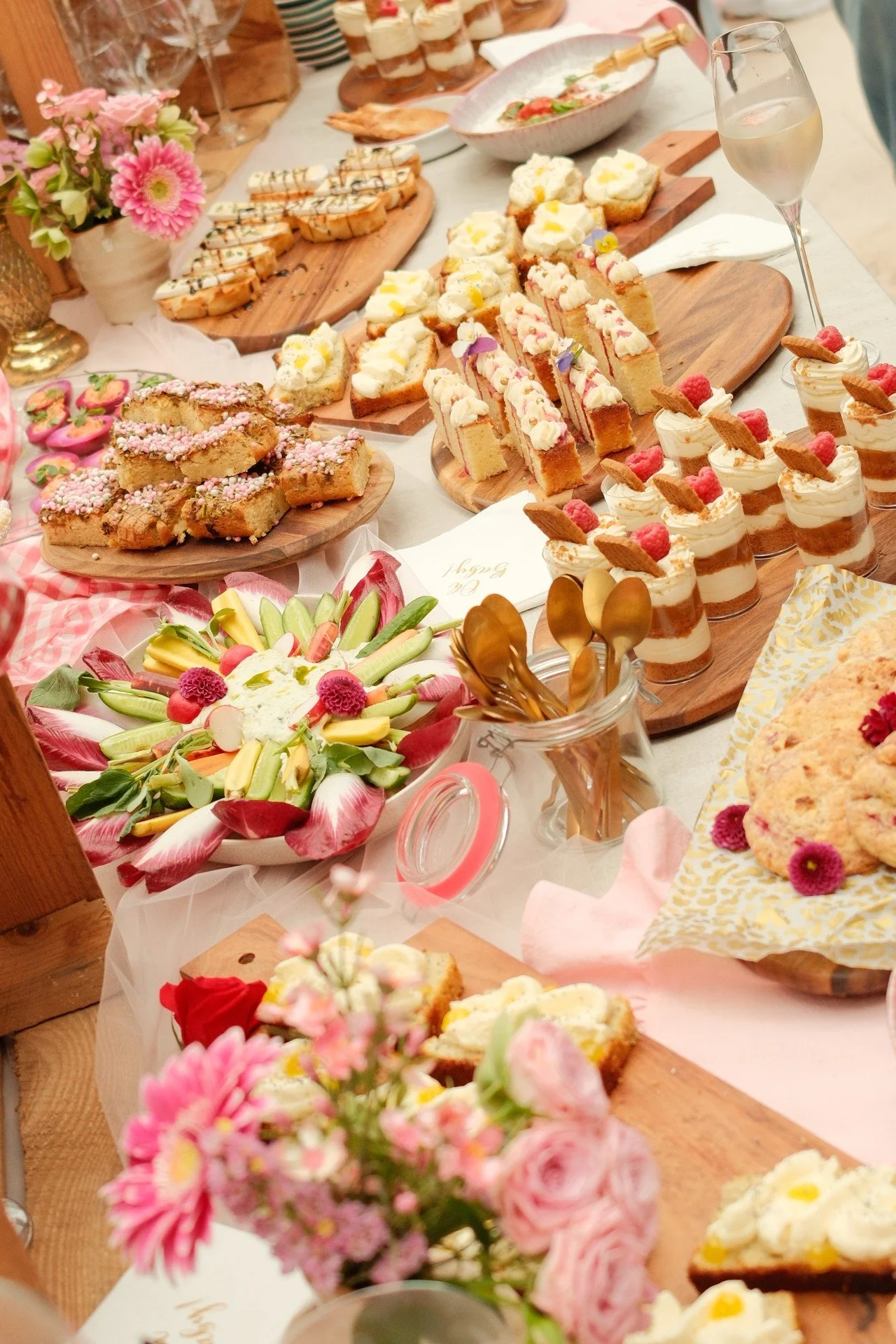 Een tafel met diverse schaal- en toetjehapjes, bloemen en glazen wijn op een feestelijk buffet.