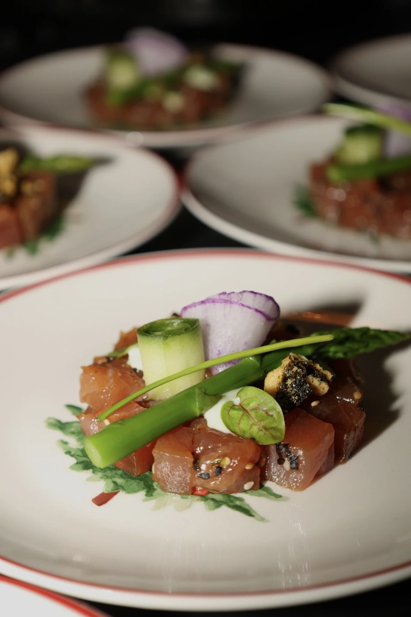 Close-up van een gerecht met rauwe zalm, groene ui, radijsjes en zwarte sesamzaadjes op een decoratief bord.