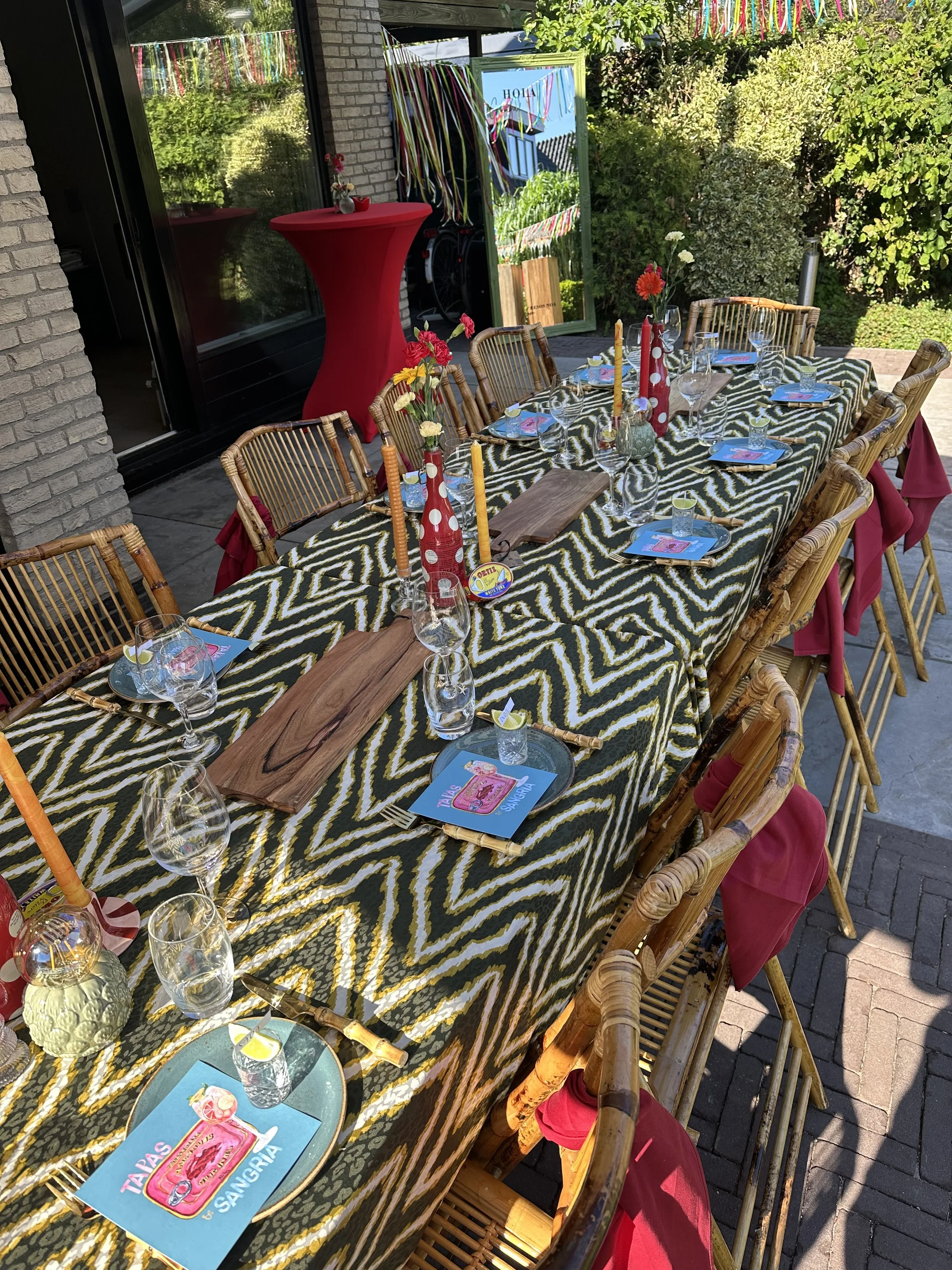 Tafels klaar voor een feest, met bloemen, kaarsen, wijn, en tafelkaarten, buiten in de tuin.