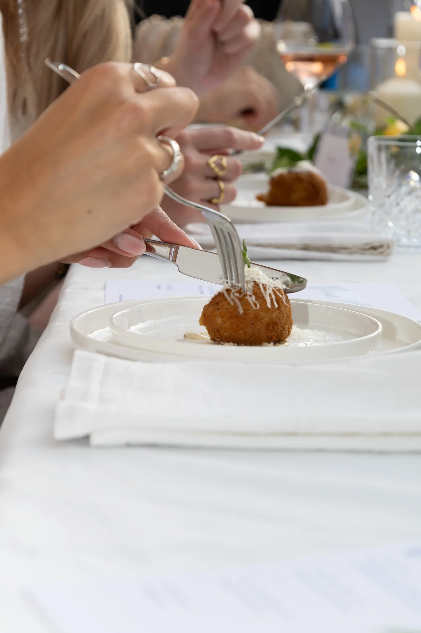 Close-up van een gerecht met een kroket en kaas. Mensen met sieraden eten in de achtergrond.