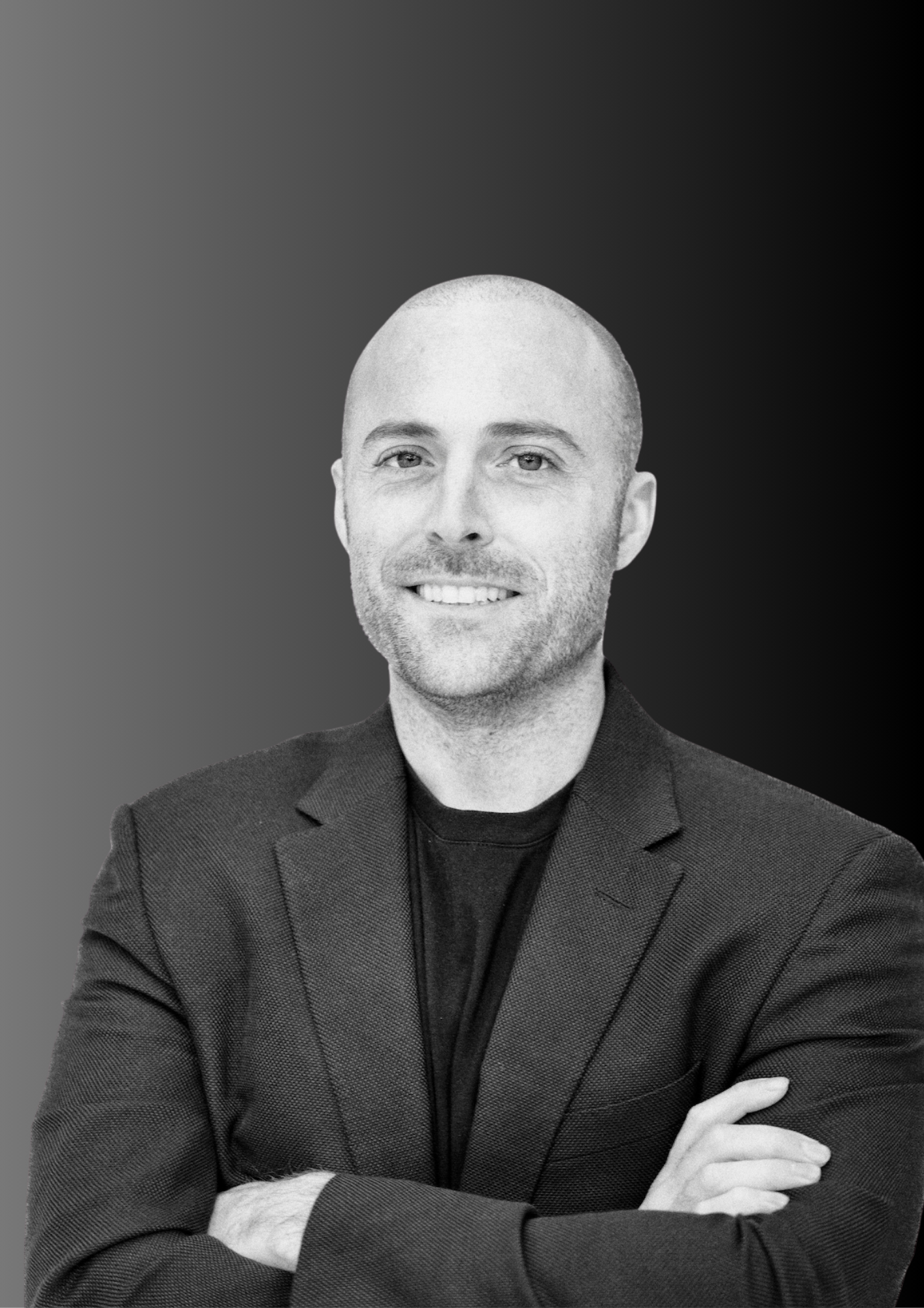 Black and white portrait of a man with a shaved head and beard, smiling, wearing a dark blazer and shirt, with arms crossed, against a gradient background.