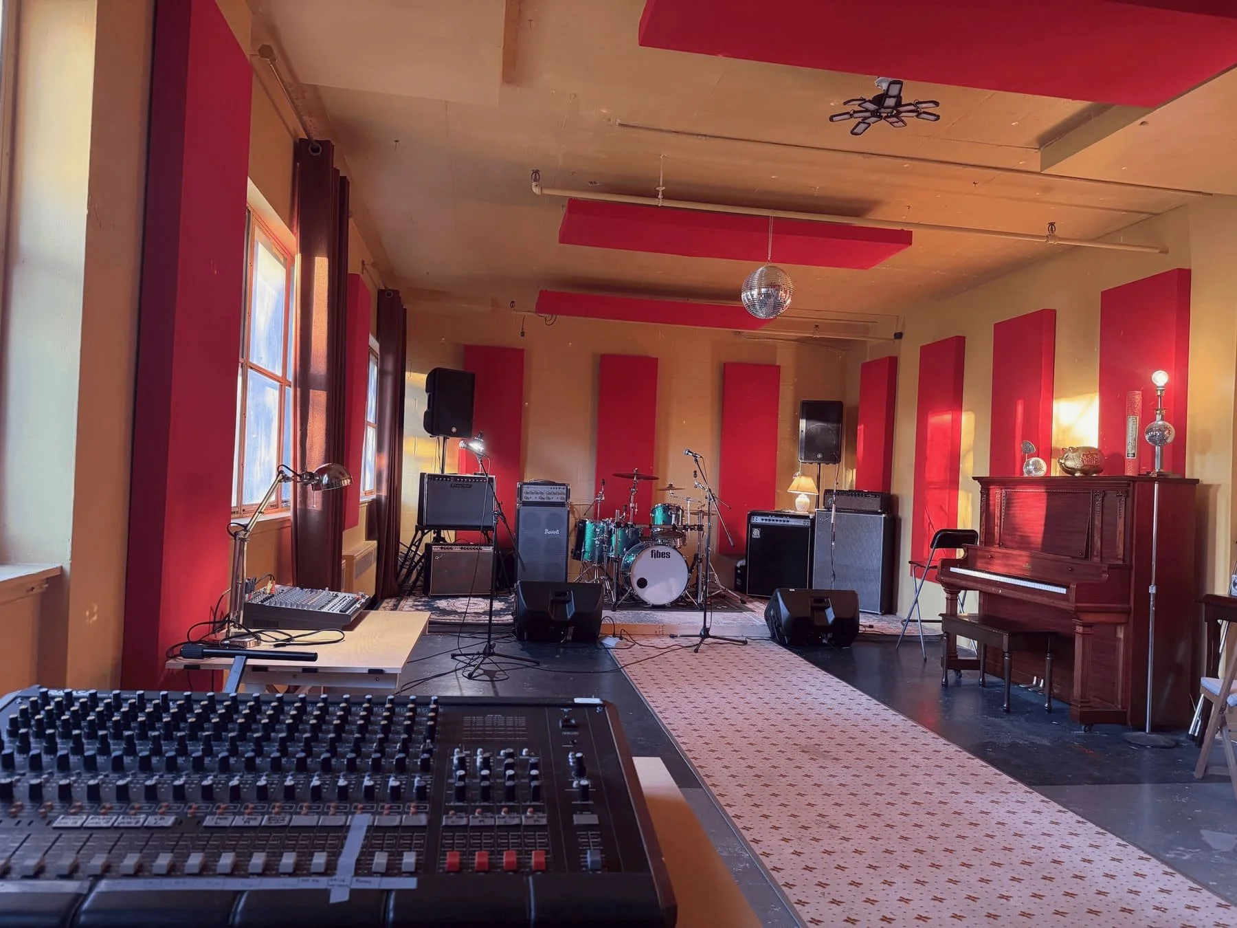 Bright rehearsal room at NOW Studio Montreal with drums, amps, red acoustic panels and large windows