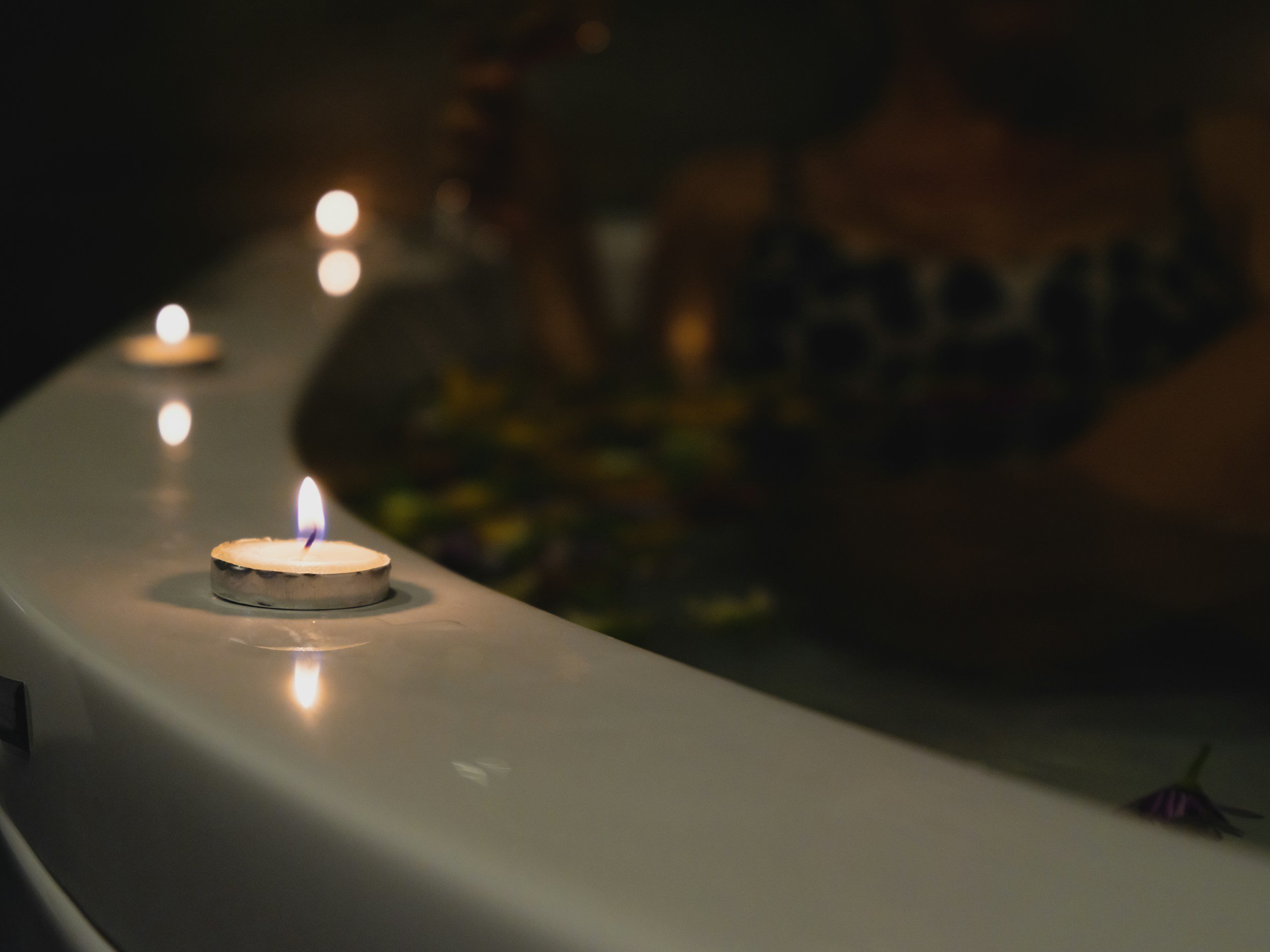 Close-up of a small candle burning on a white surface with a background of colorful, blurry lights.