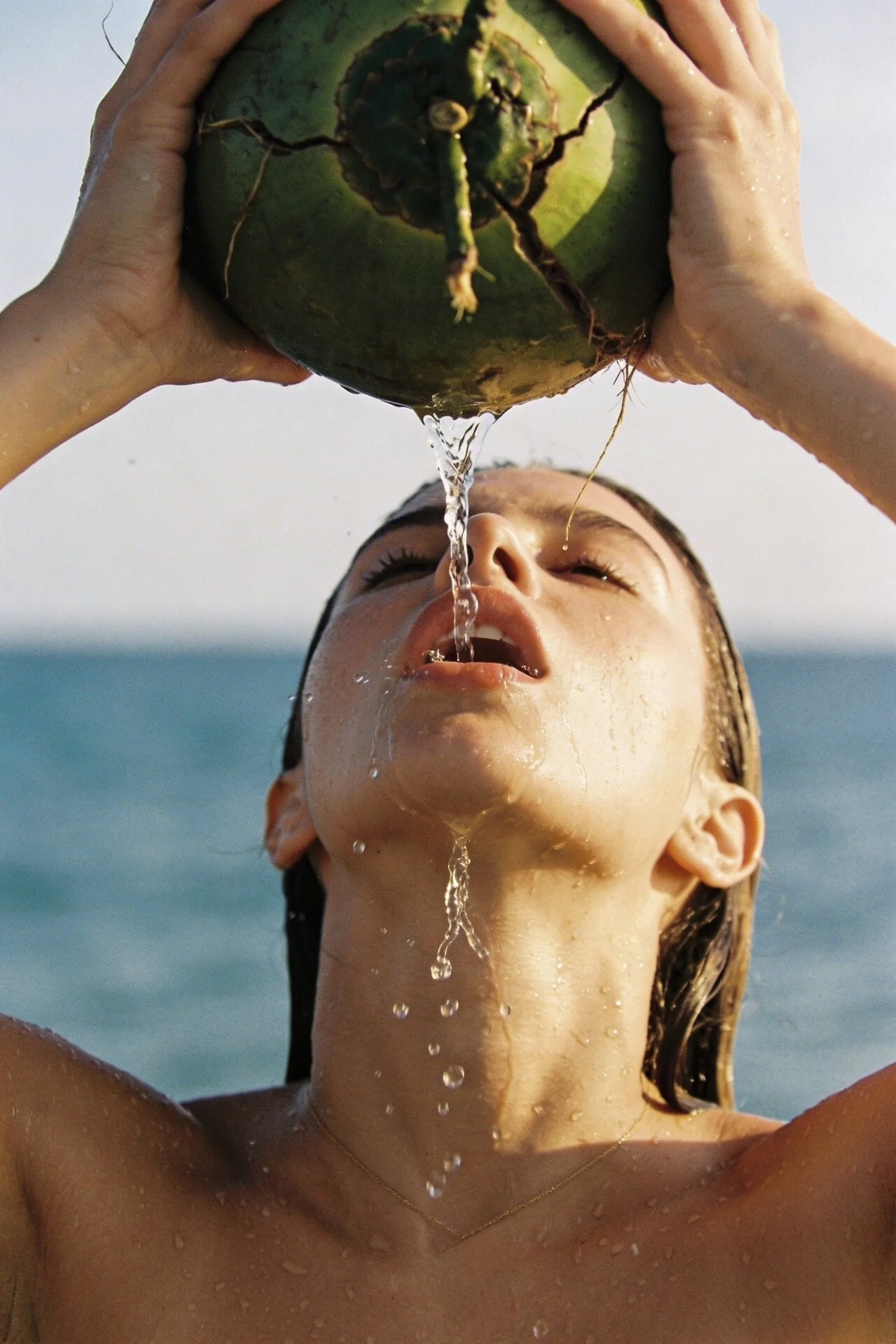Person pouring water from a coconut into their mouth at the beach.