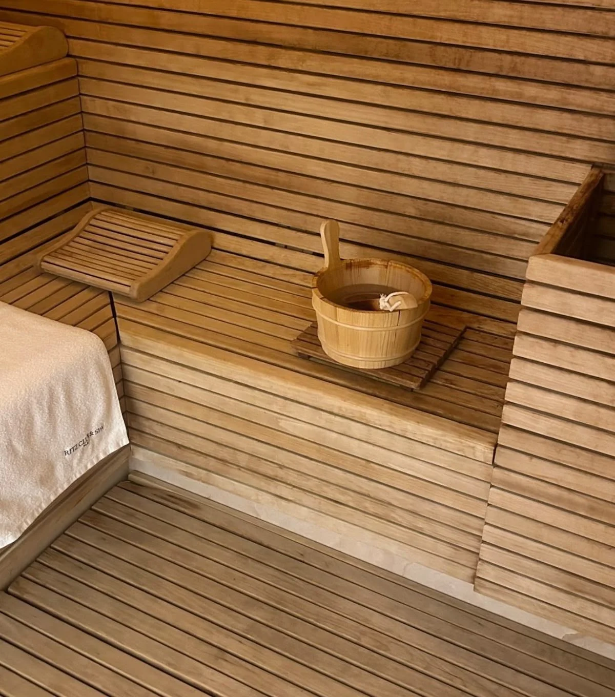 Wooden sauna room with a towel, a bench, and a bucket of water with a ladle.