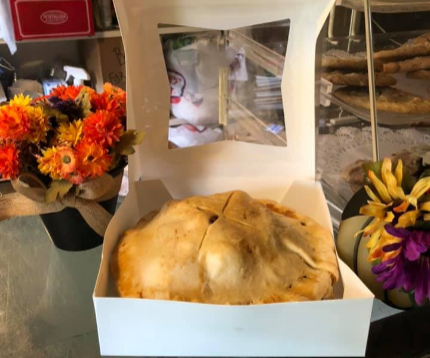 A cat looking out through a glass window inside a food takeout box, with flowers in the background.