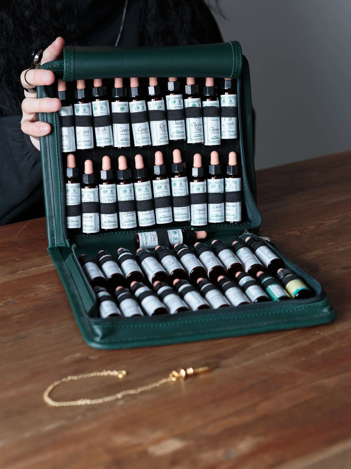 Open green case containing small bottles of essential oils with droppers, placed on a wooden table.