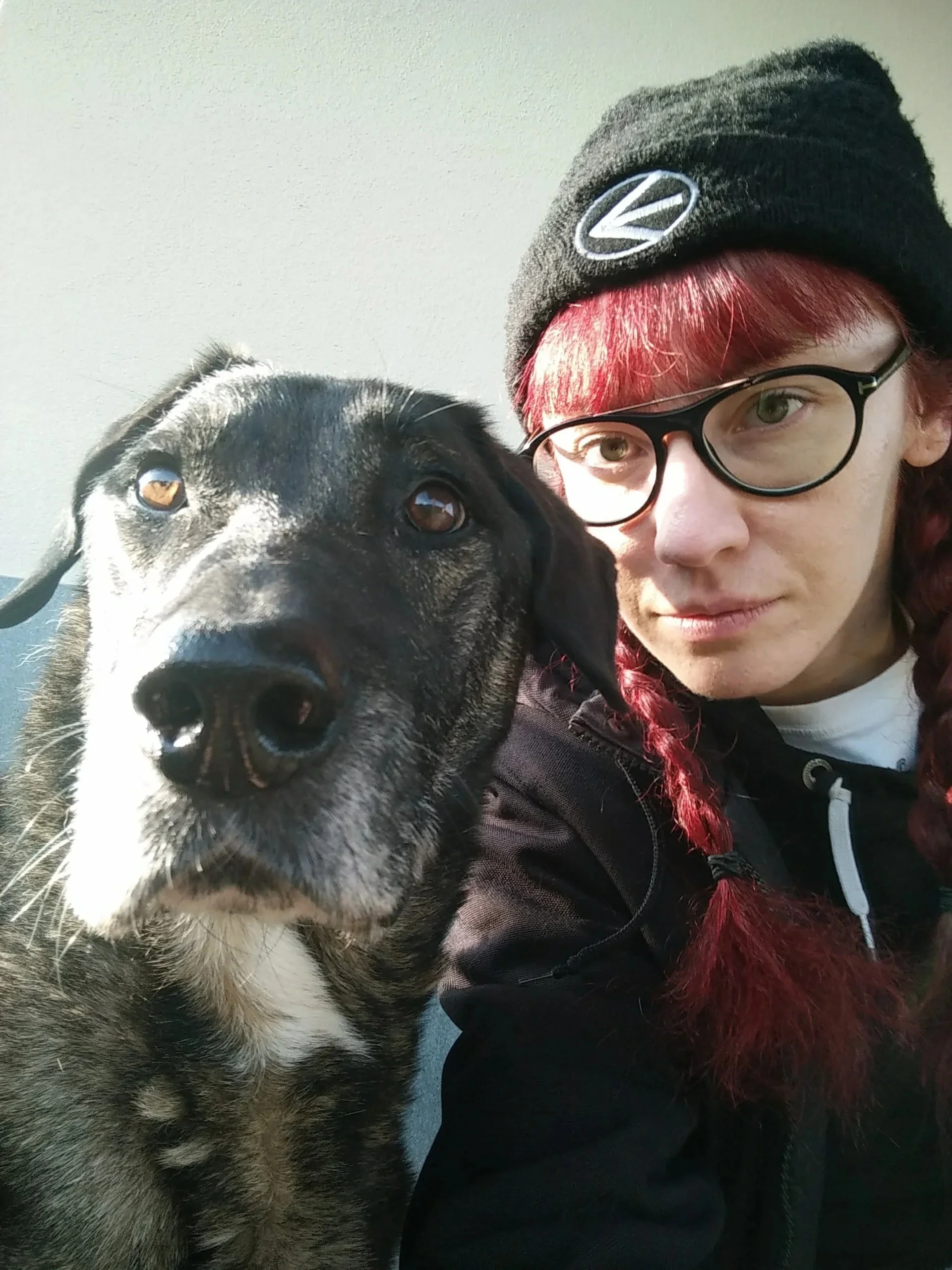 Person with red hair and glasses taking a selfie with a black and white dog.