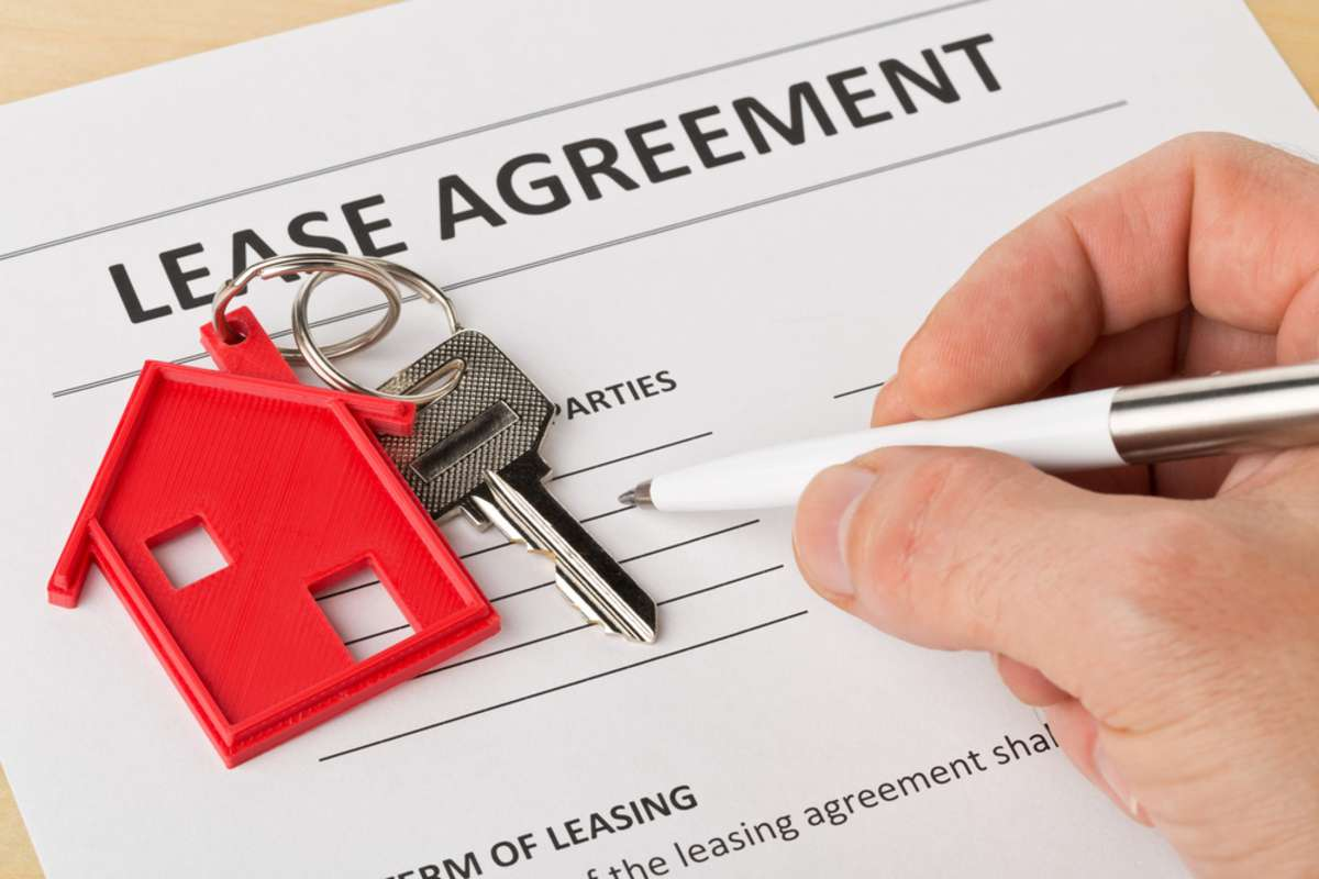Hand signing a lease agreement with a house-shaped keychain on top of the paper.