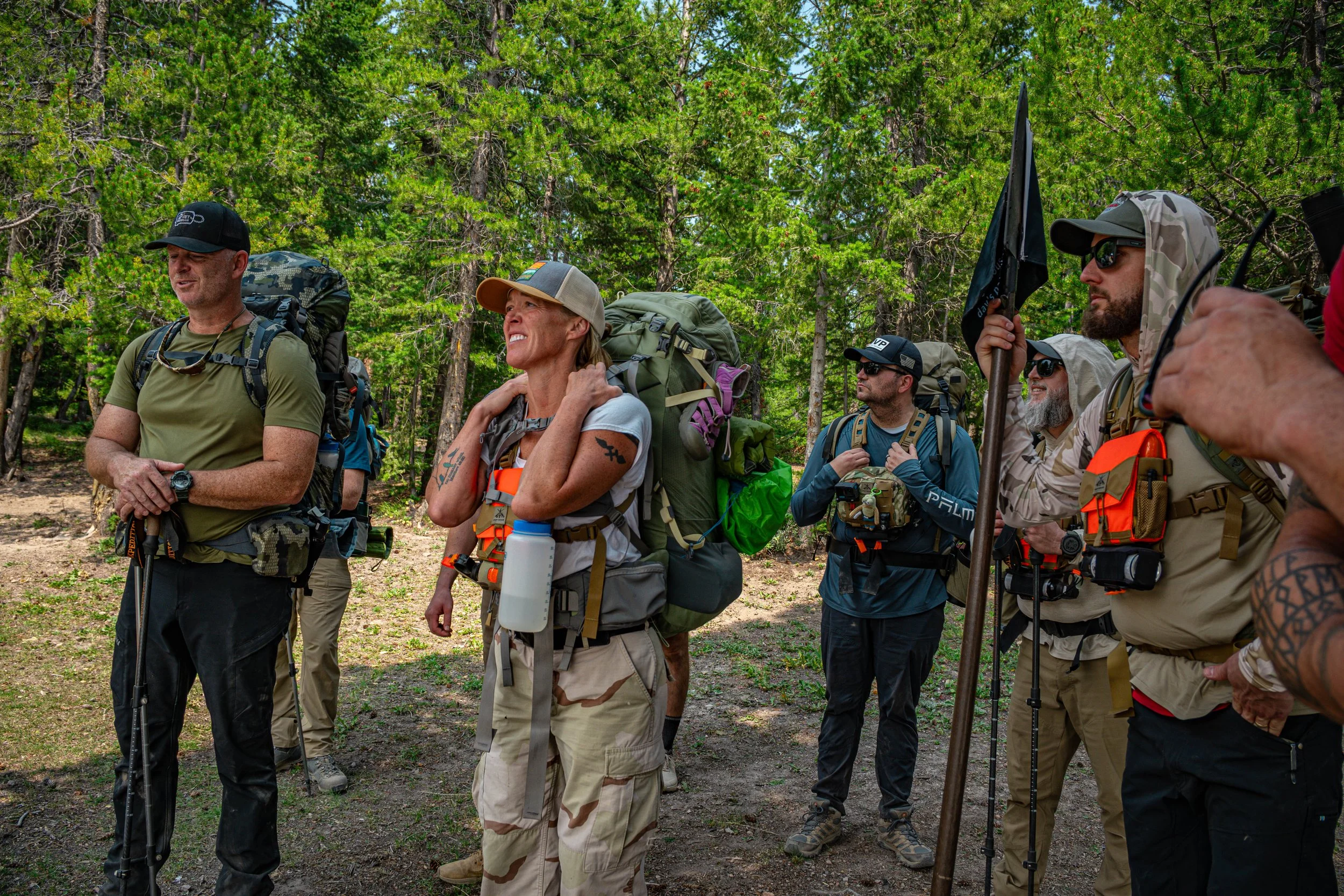 Group of hikers standing in a forest, wearing backpacks and outdoor gear.