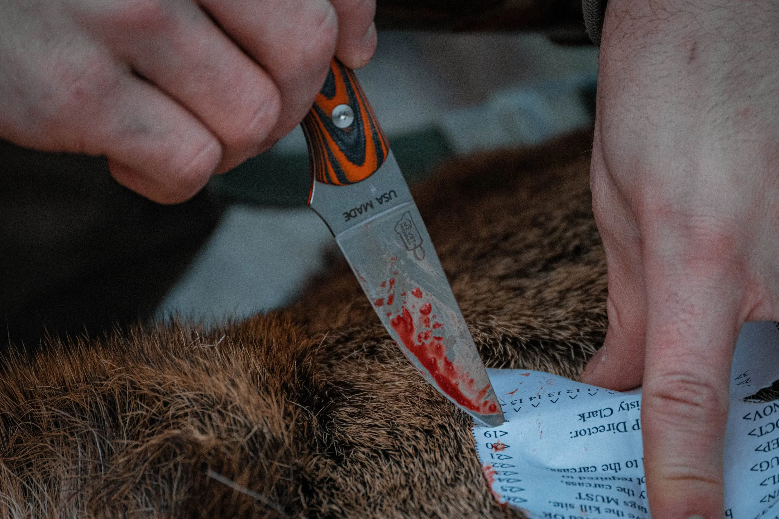 Person holding a blood-stained knife while working on a patient, with a medical chart on the ground.